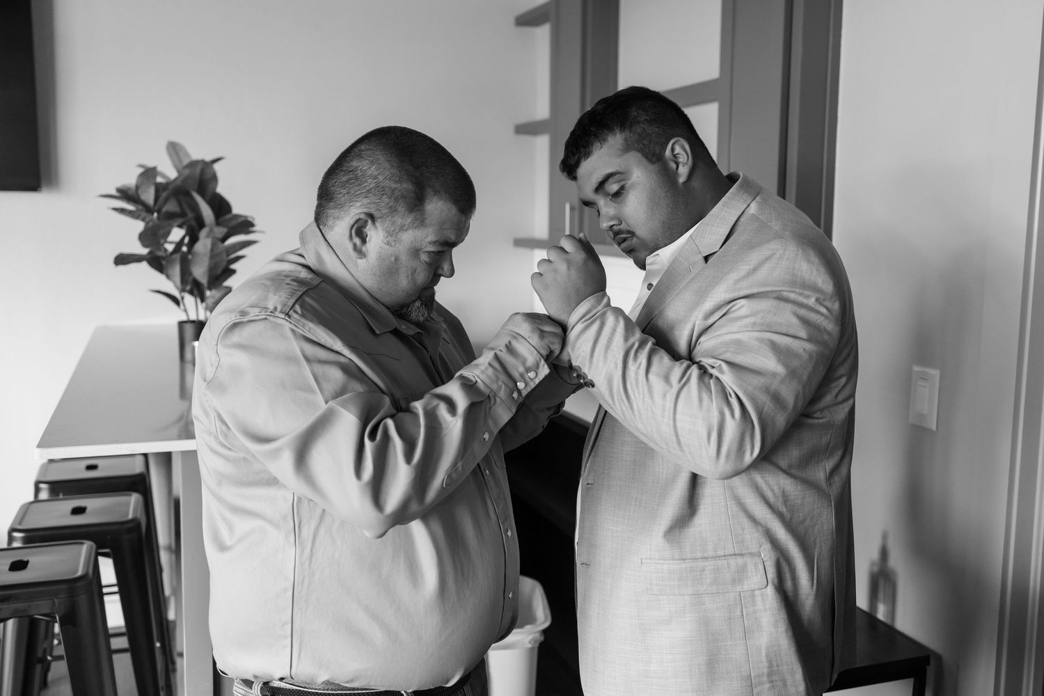 Two men in suits helping each other with boutonnieres in a black and white Oklahoma wedding preparation photo.
