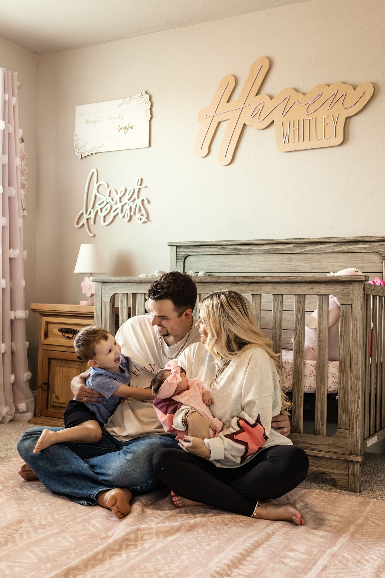 Family sitting on nursery floor with baby girl, toddler son, and wooden name sign at a family session in Oklahoma. in home photography.