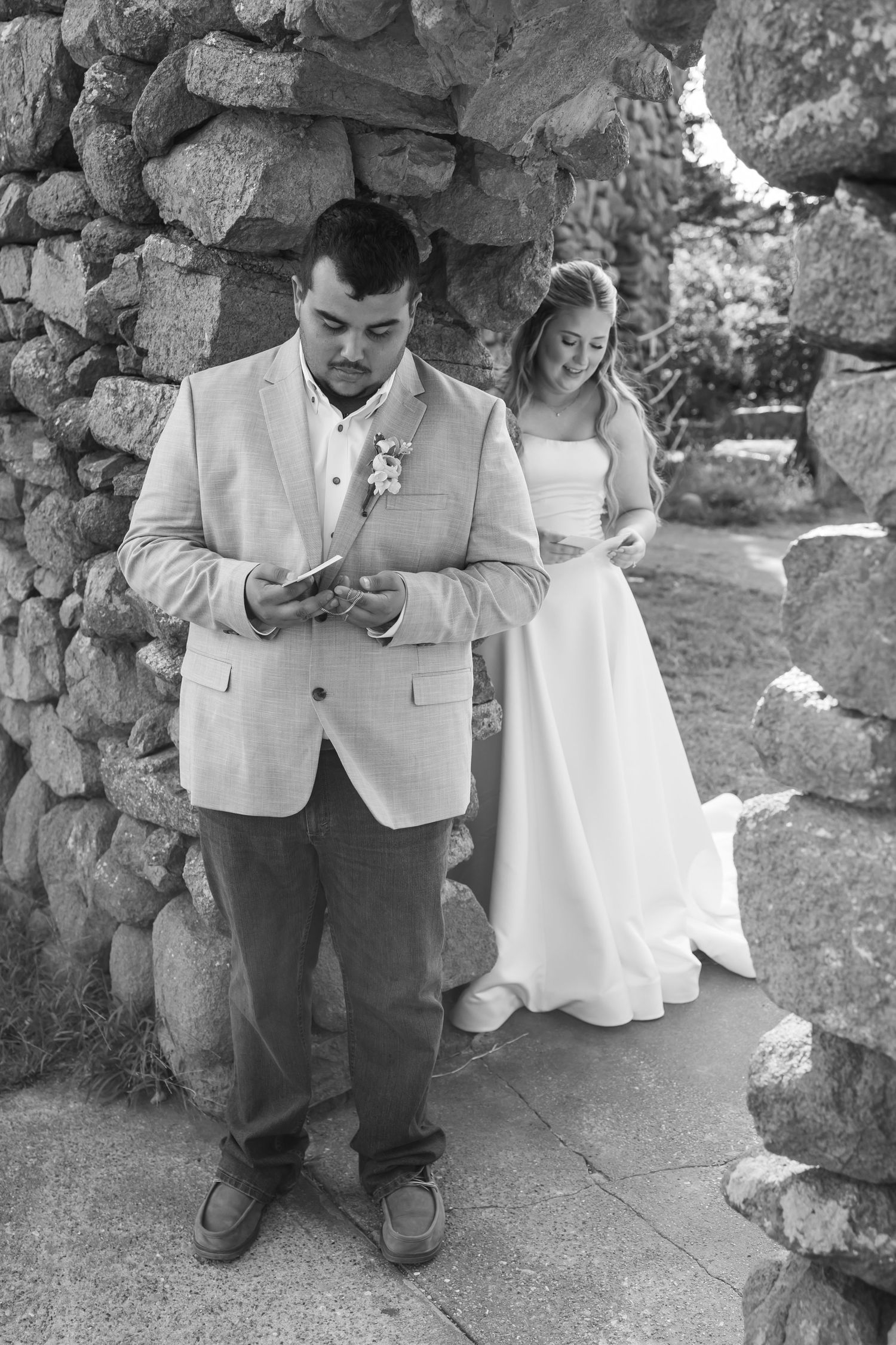 Black and white photo of Oklahoma bride and groom reading wedding vows separately near a stone wall before ceremony.