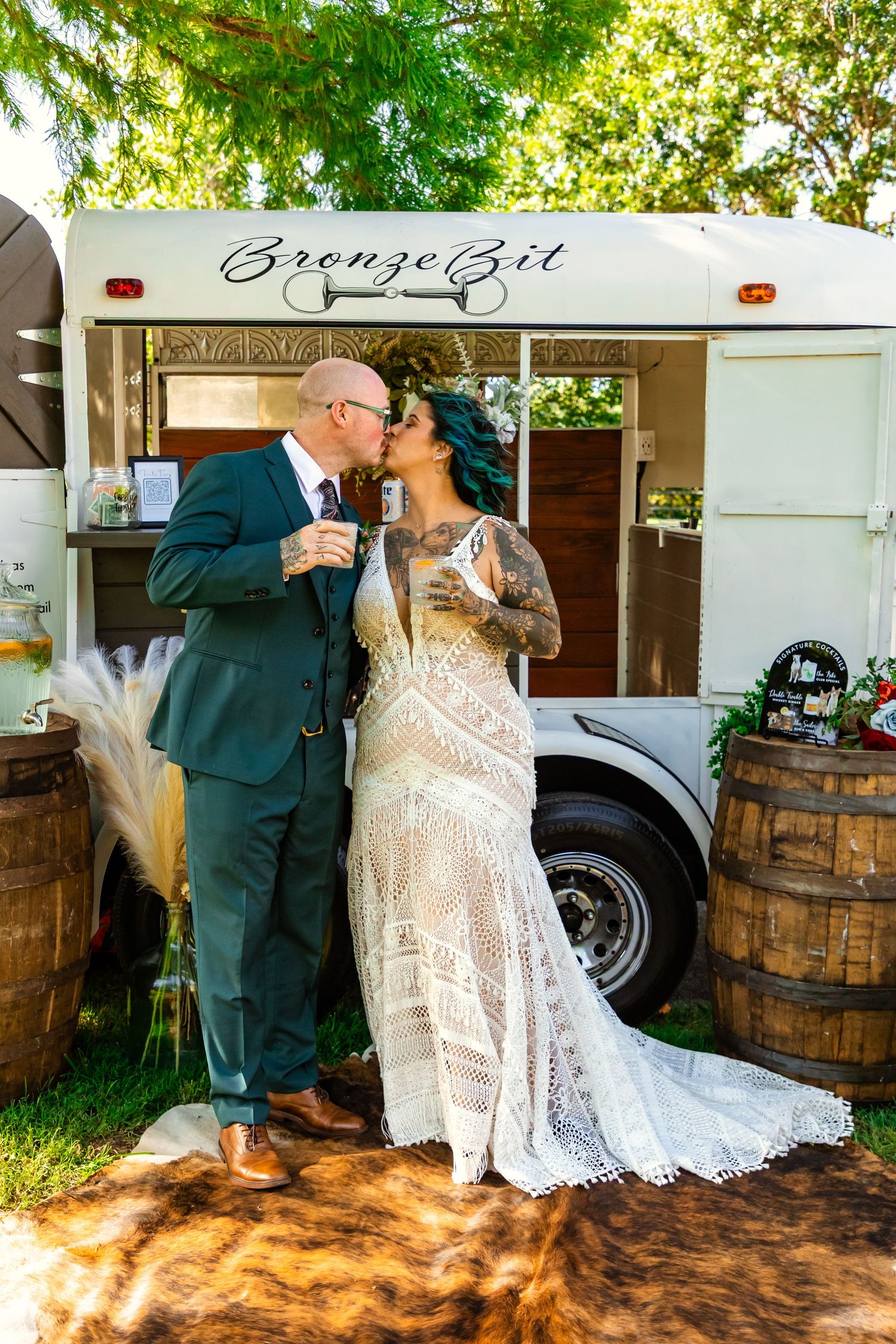 Bride and groom kissing in front of a white vintage bartending trailer at an outdoor wedding reception in Weatherford, Oklahoma