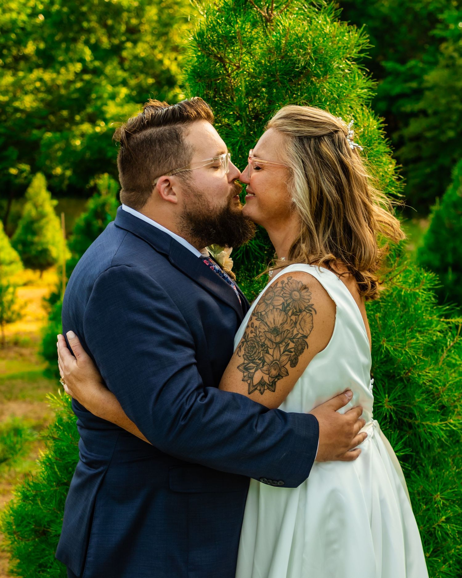 Couple sharing a romantic kiss in wedding attire at wells Christmas tree farm in Norman, Oklahoma, bride in white dress with floral tattoo.