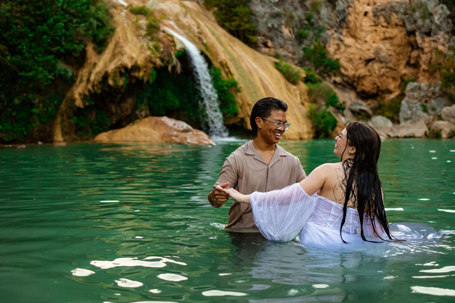 Wedding couple enjoying a romantic swim in a turquoise natural pool with a turner falls waterfall and rocky cliffs in the background.