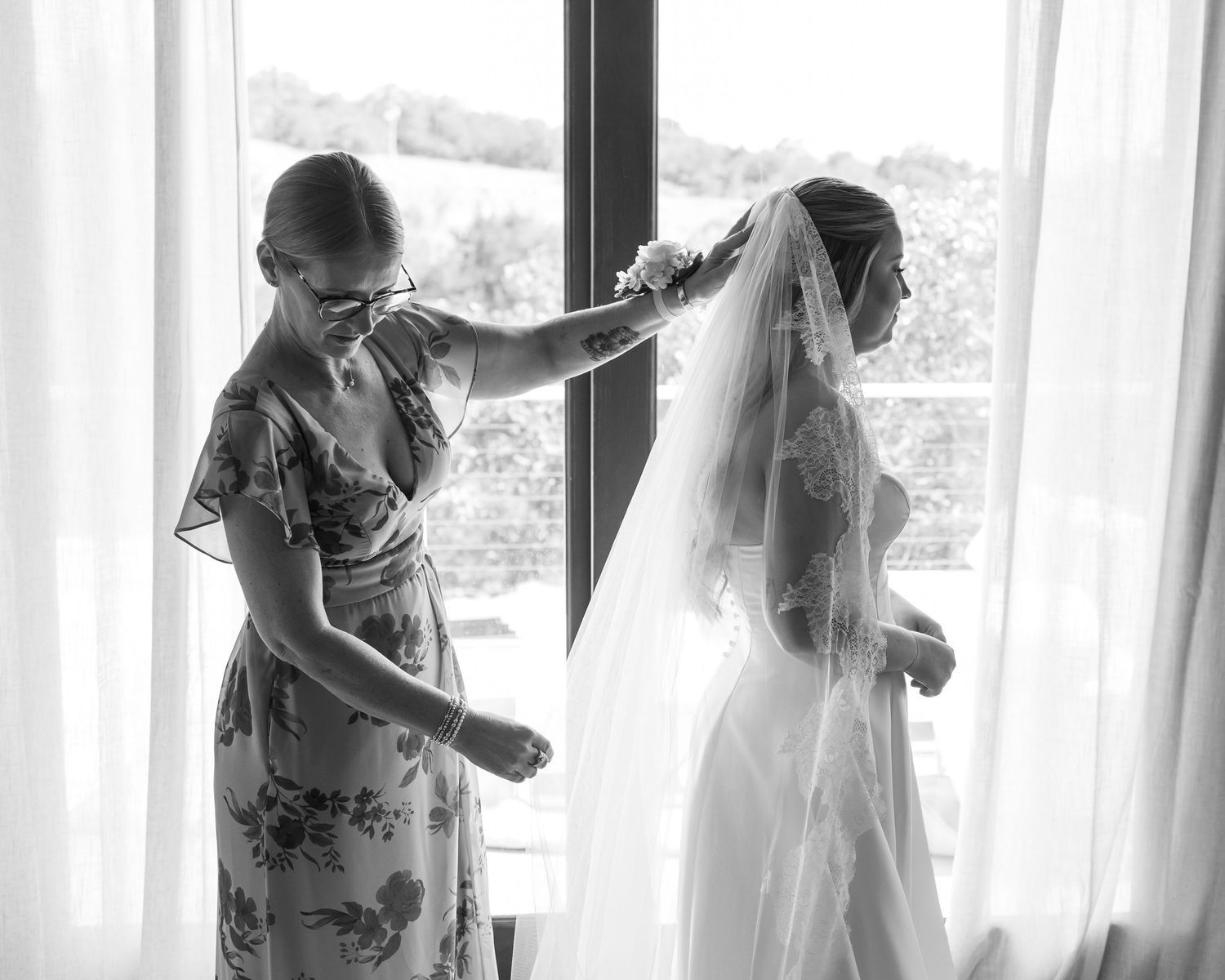 Black and white photo of a mother helping an oklahoma bride adjust her veil near a bright window on her wedding day.