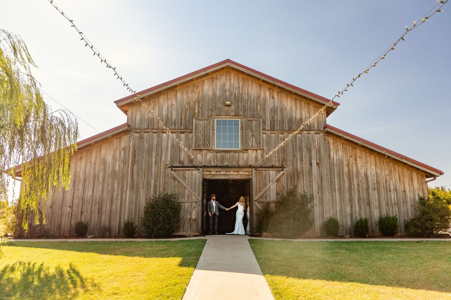 Bride and groom holding hands at entrance of rustic wooden barn wedding venue on sunny day at rustic rose ranch in Guthrie, oklahoma