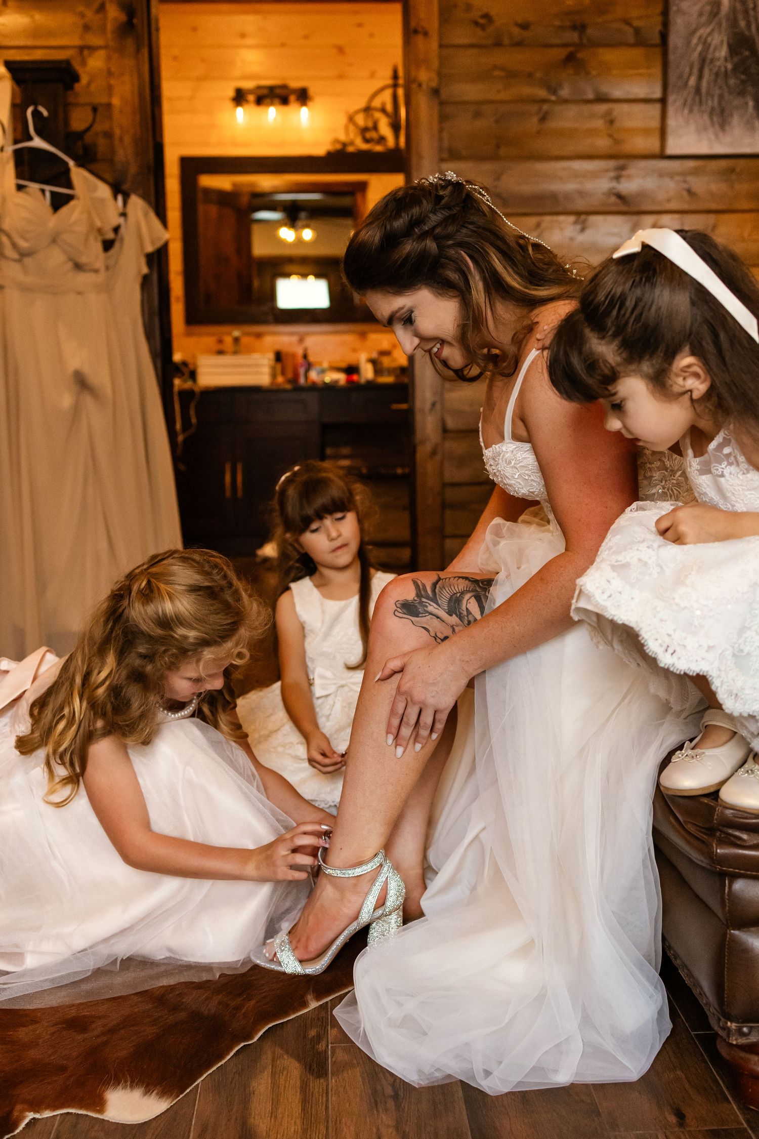 Bride in white lace gown gets teal heels put on by flower girls in rustic wood cabin bridal suite in broken bow Oklahoma elopement.