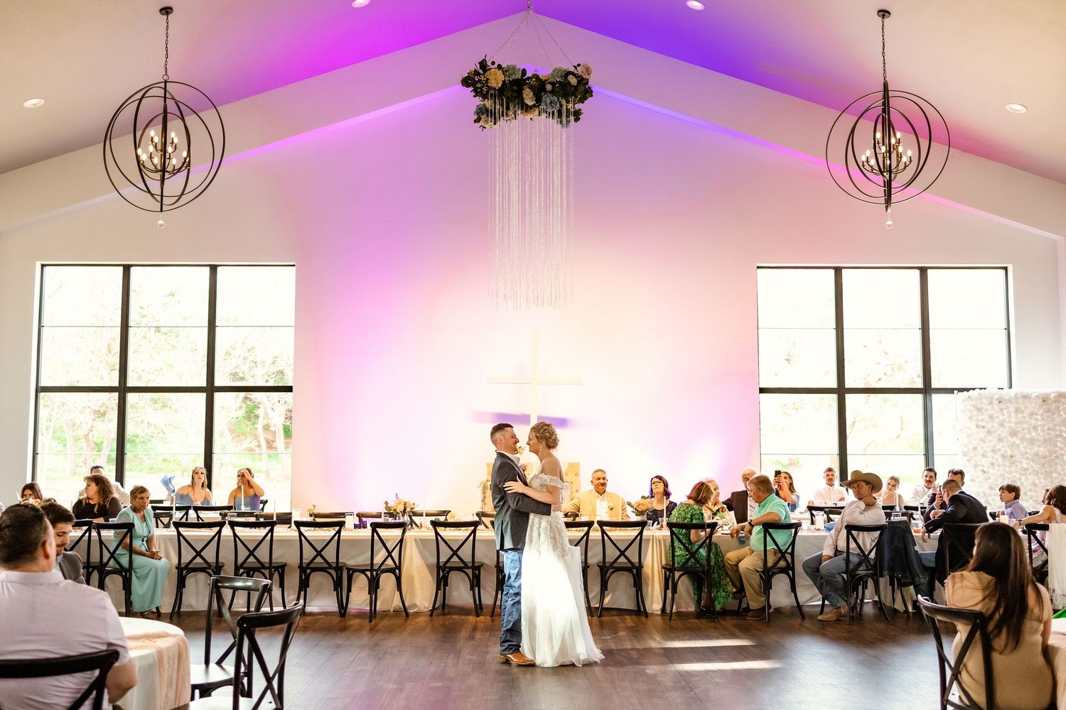 Couple shares first dance at Sorelle in Thomas, ok with purple uplighting, chandelier decor, and seated guests at long reception tables.