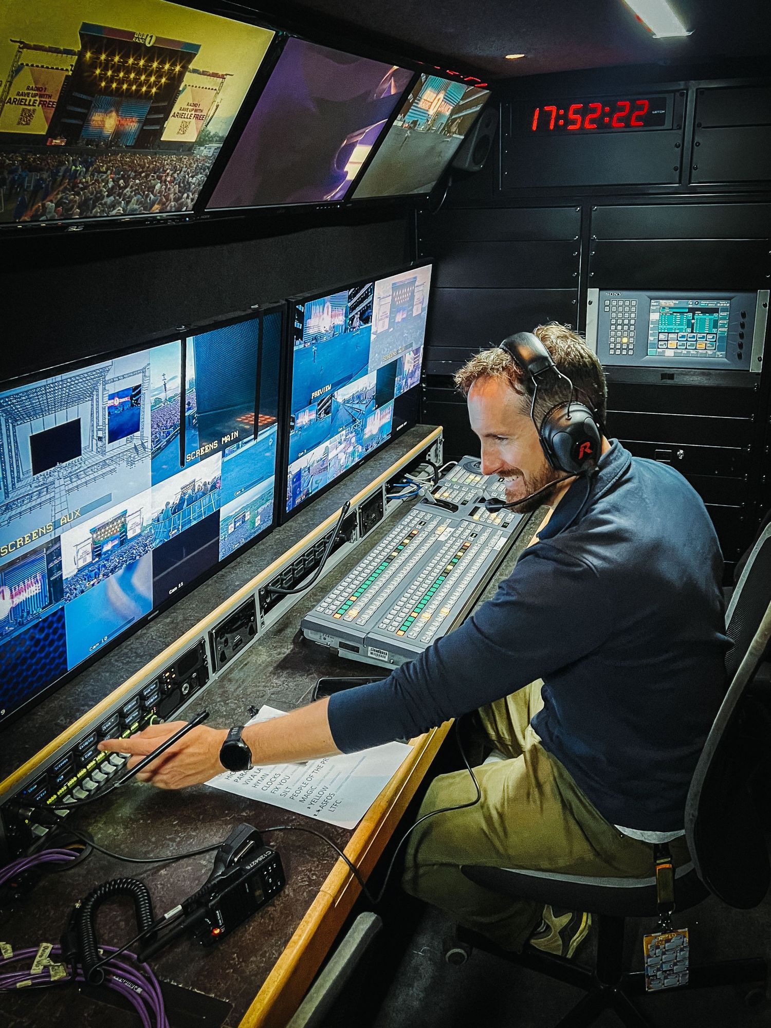 Ant Barrett (Resolve Film) with multiple faders and screens in a dimly lit broadcast control room at Radio 1 Big Weekend with Coldplay.