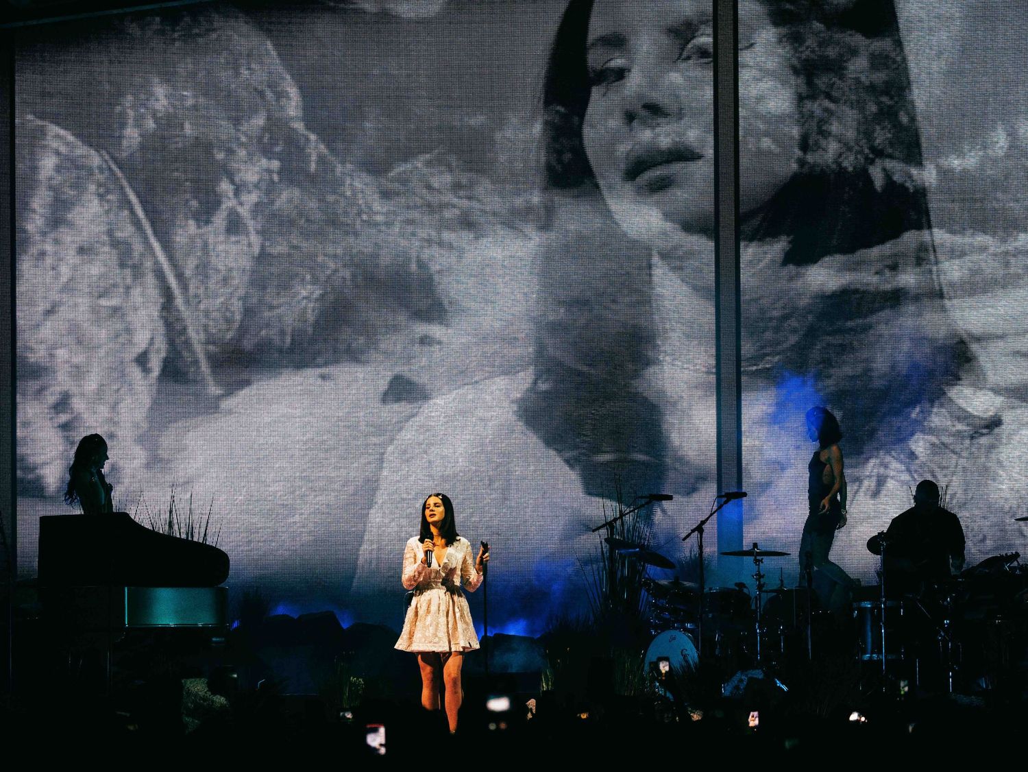 Concert performer Lana Del Rey in a white dress on stage with dramatic backdrop projections, directed by Ant Barrett (RESOLVE FILM)
