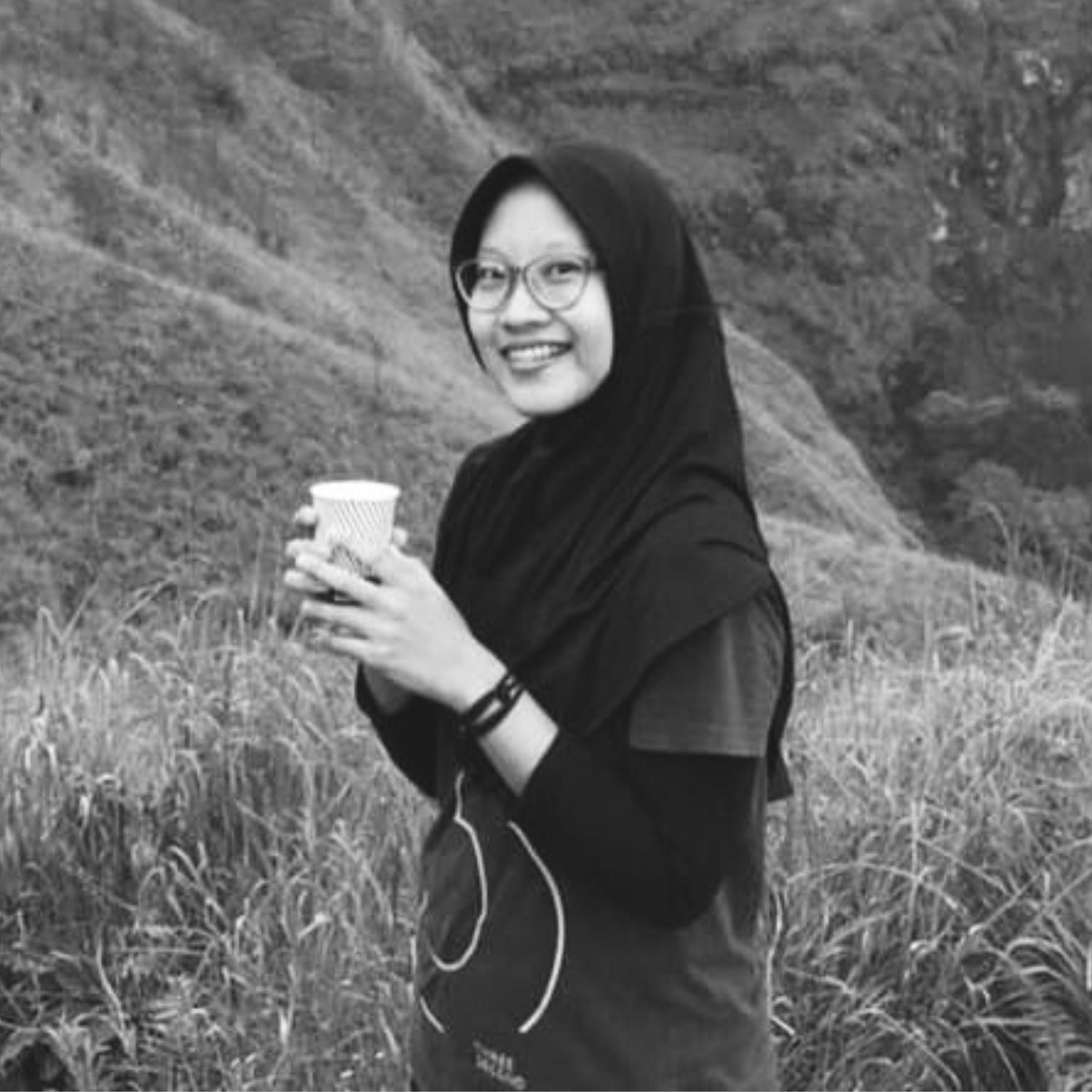 Person holding beverage poses against mountain landscape backdrop.