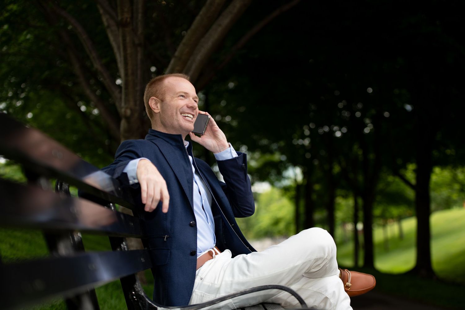 A series of candid photos show someone in a navy suit sitting and laughing while outdoors in a park setting.
