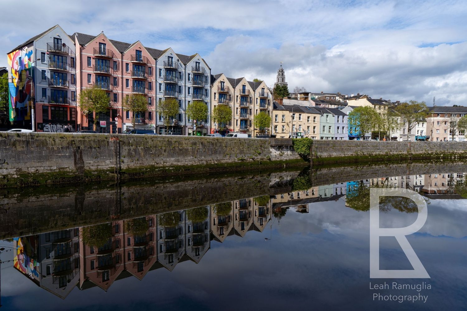 Colorful waterfront buildings in Cork, Ireland reflect perfectly in the calm River Lee on a cloudy day.