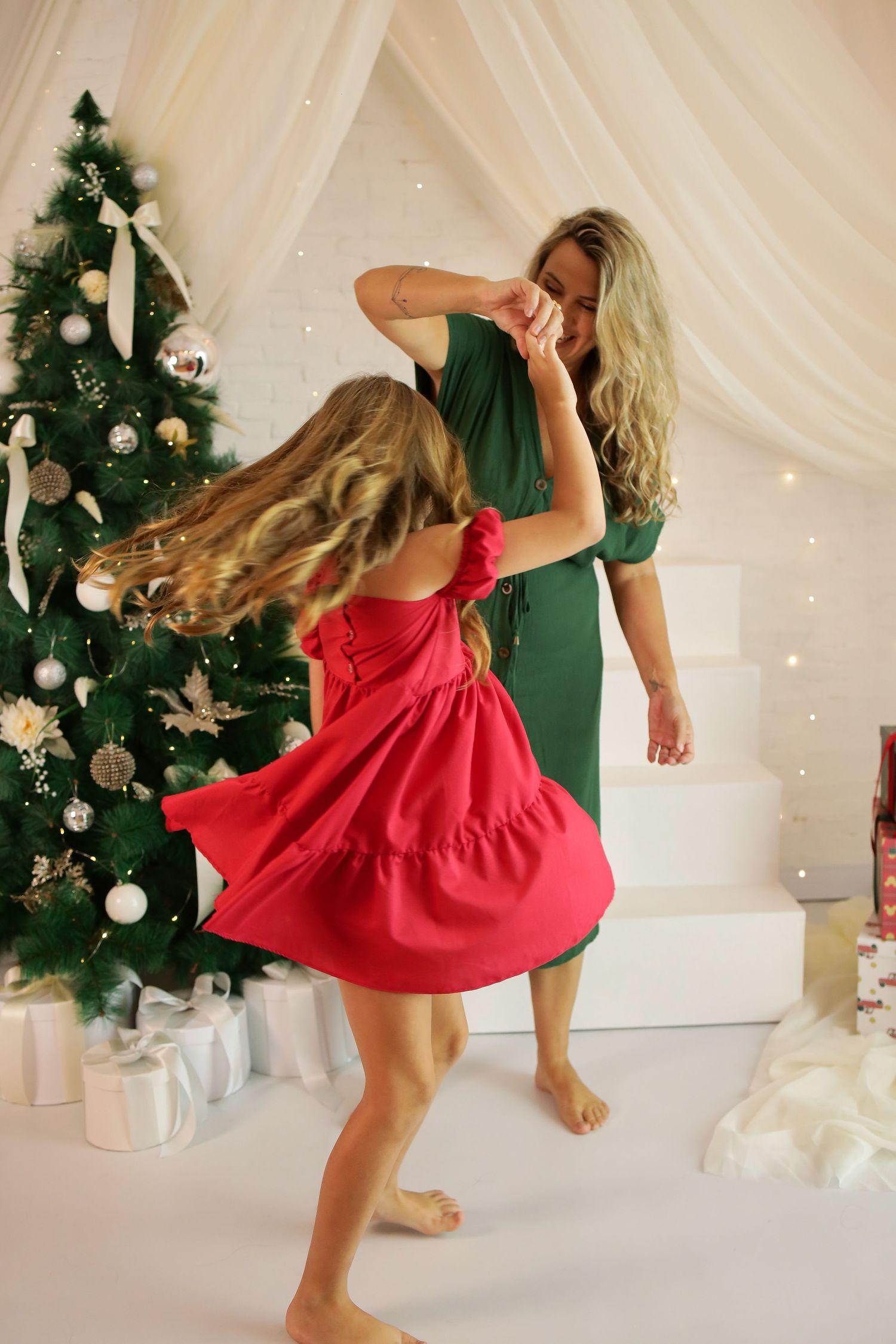 A dancer in a red dress twirls gracefully in front of a decorated Christmas tree and white backdrop.