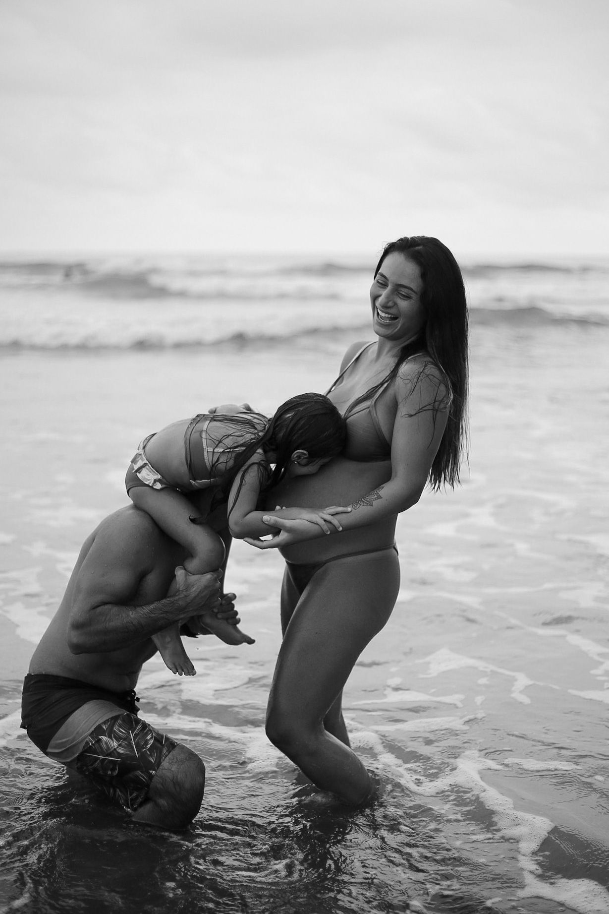 A couple shares a tender moment kissing in the ocean waves, captured in black and white photography.