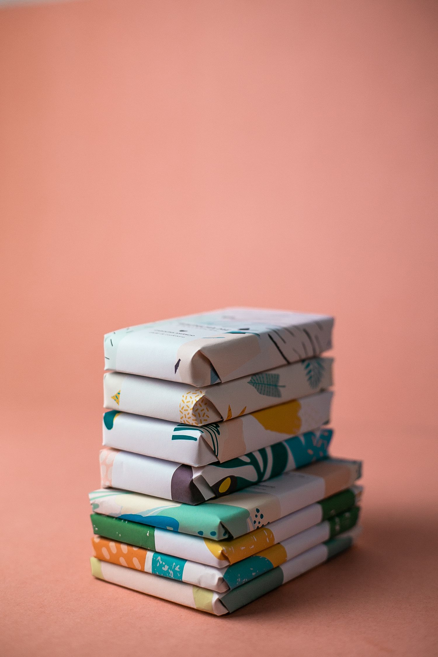 Stack of white and colorful patterned fabric squares arranged neatly against a peachy pink background.