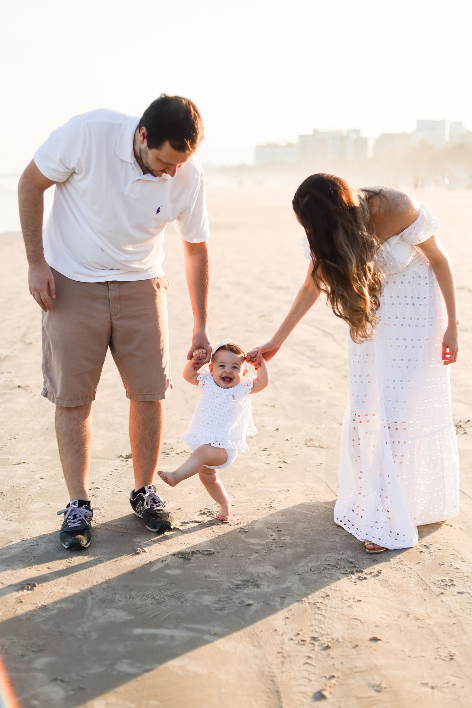 Family enjoying a sunset walk together on a sandy beach with a small child learning to walk between parents.