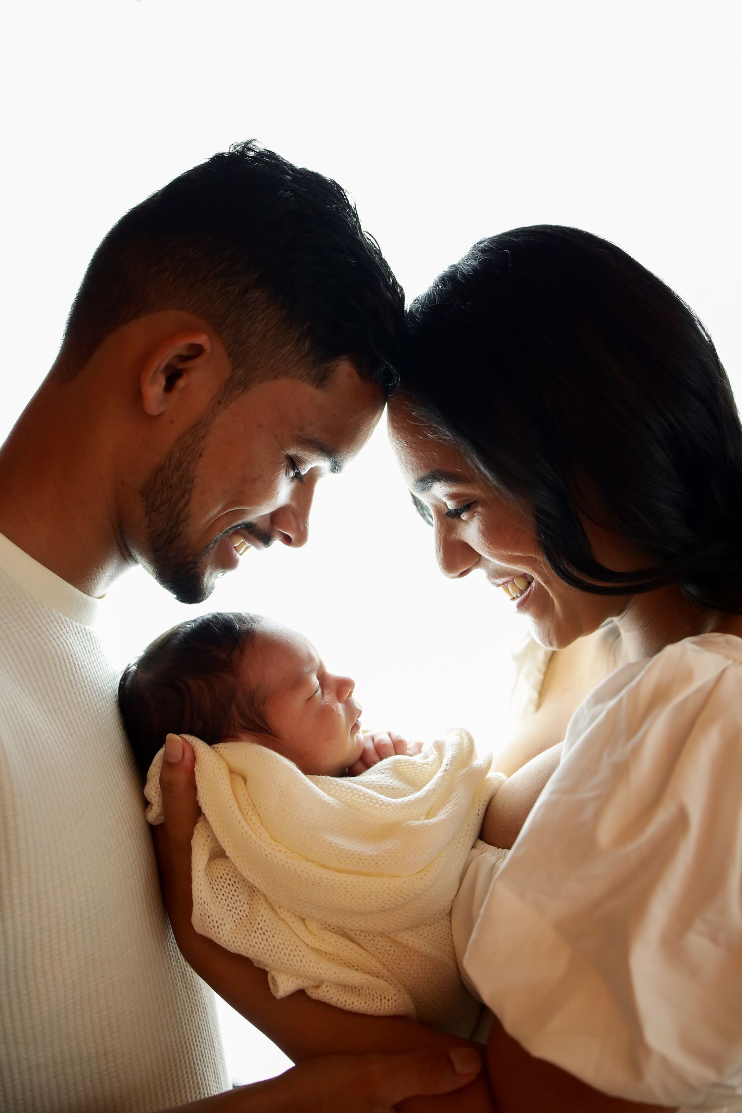 A loving family embraces their newborn baby in a tender backlit moment showing warmth and connection.