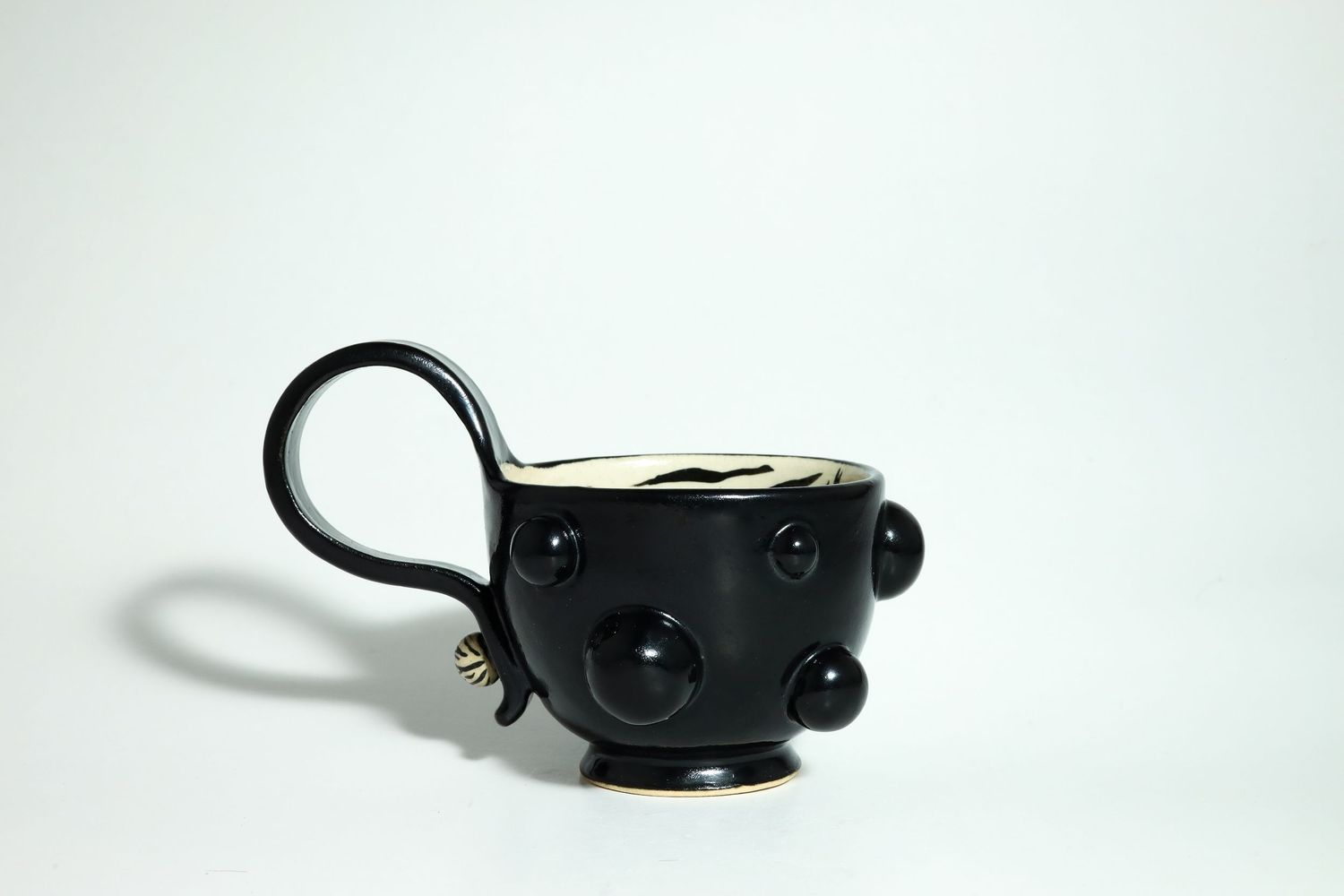 Black ceramic mug with unique button-like design elements sits against white background casting soft shadow.