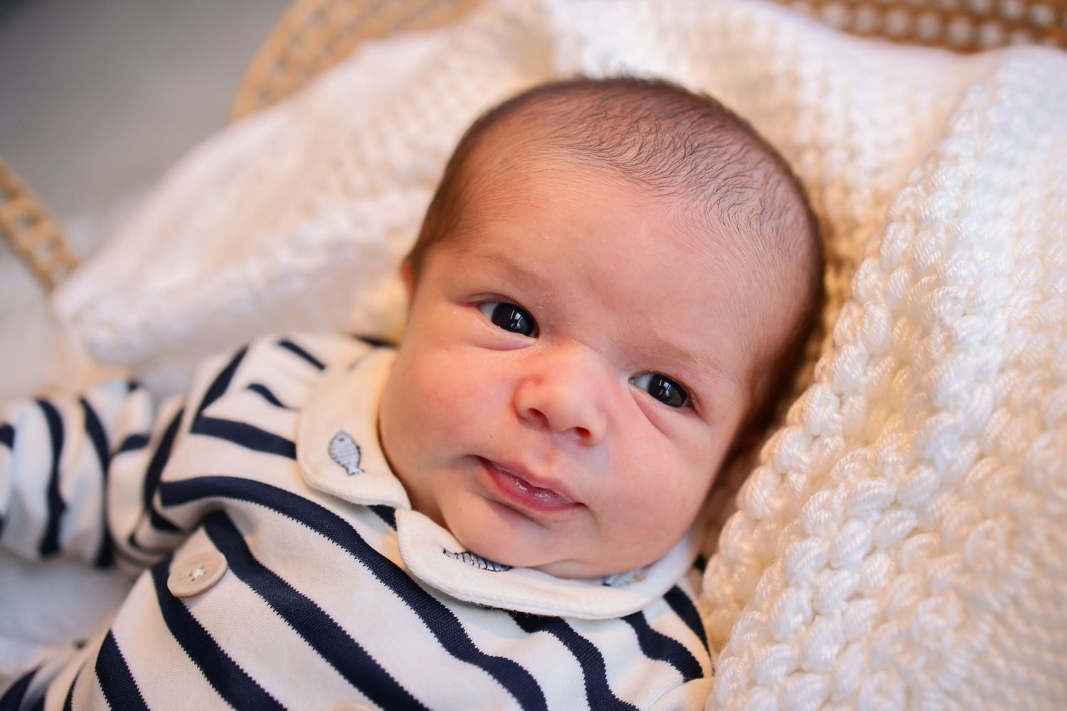 Baby wearing navy blue and white striped outfit laying on soft beige blanket background.