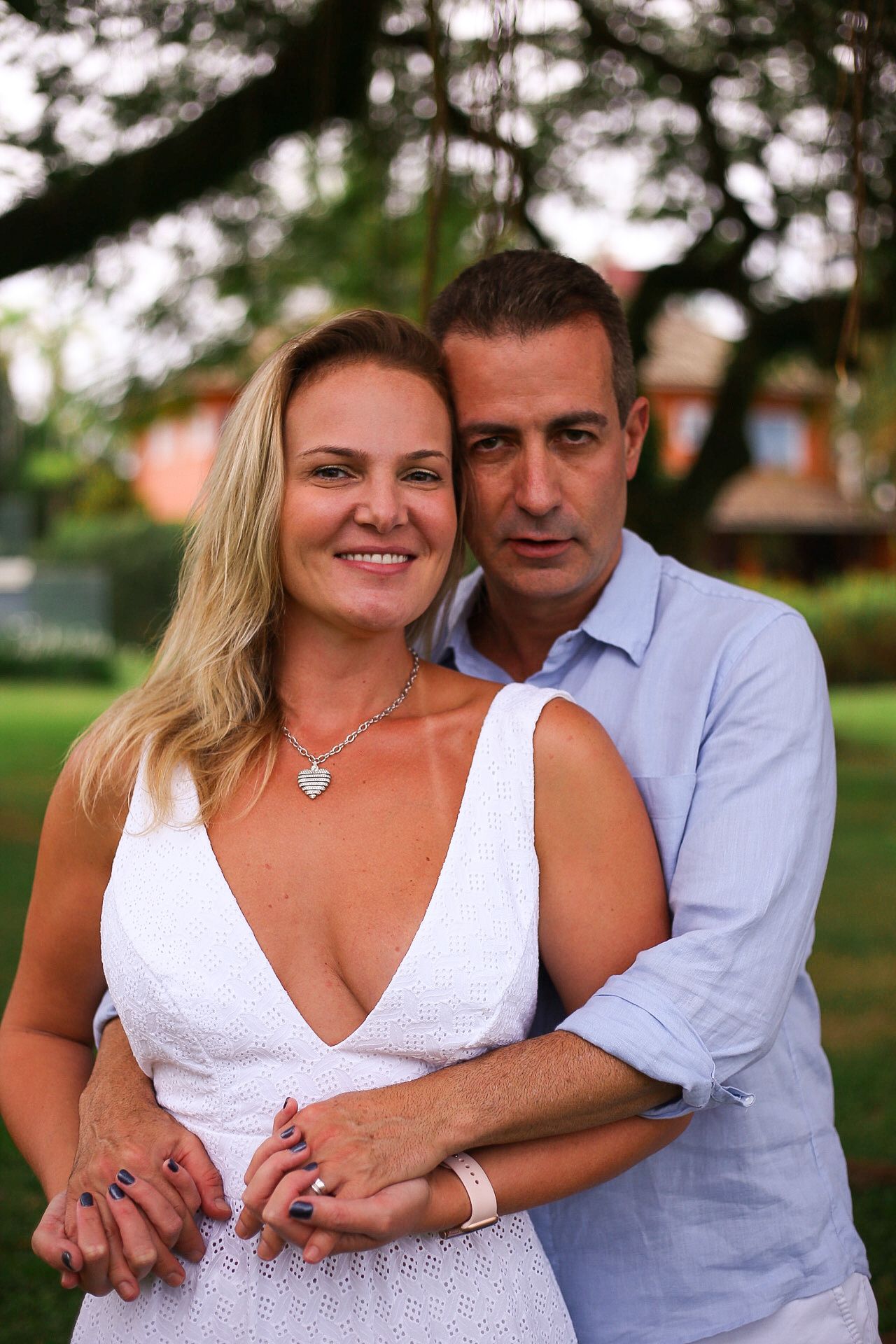 A couple in white and light blue clothing embraces while standing outdoors.