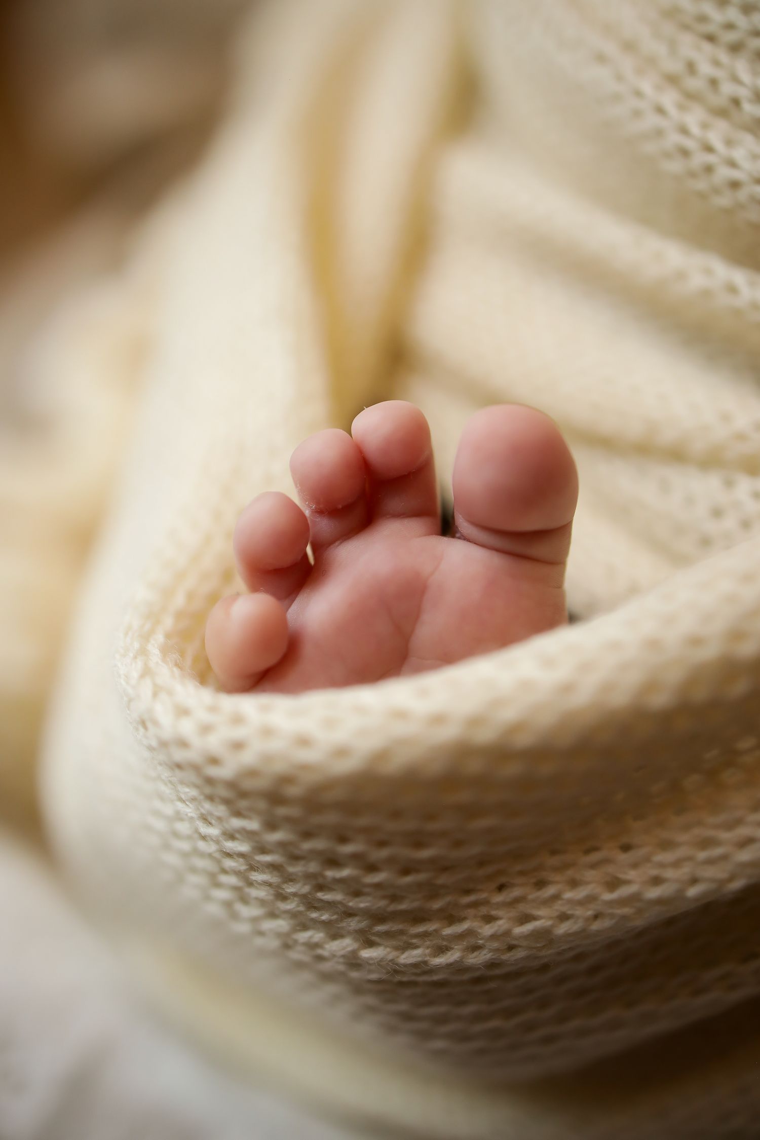 Tiny baby foot resting on soft cream-colored knitted blanket in warm natural lighting.