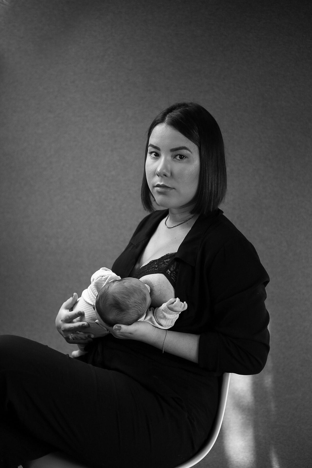 Black and white portrait of a person in dark clothing holding an infant while sitting against a simple background.