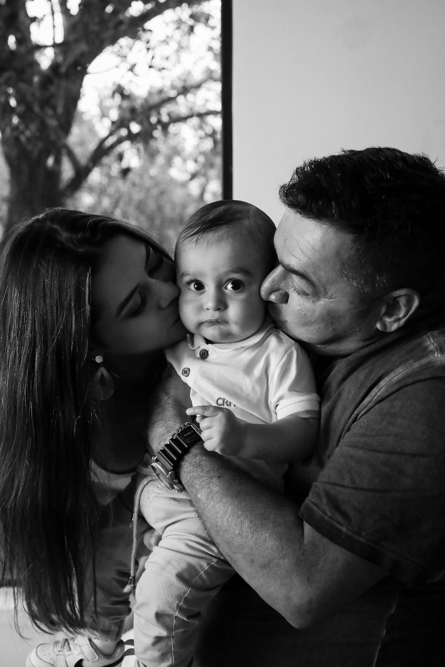 Black and white family portrait showing tender moment between parents and their young baby against a blurred background.