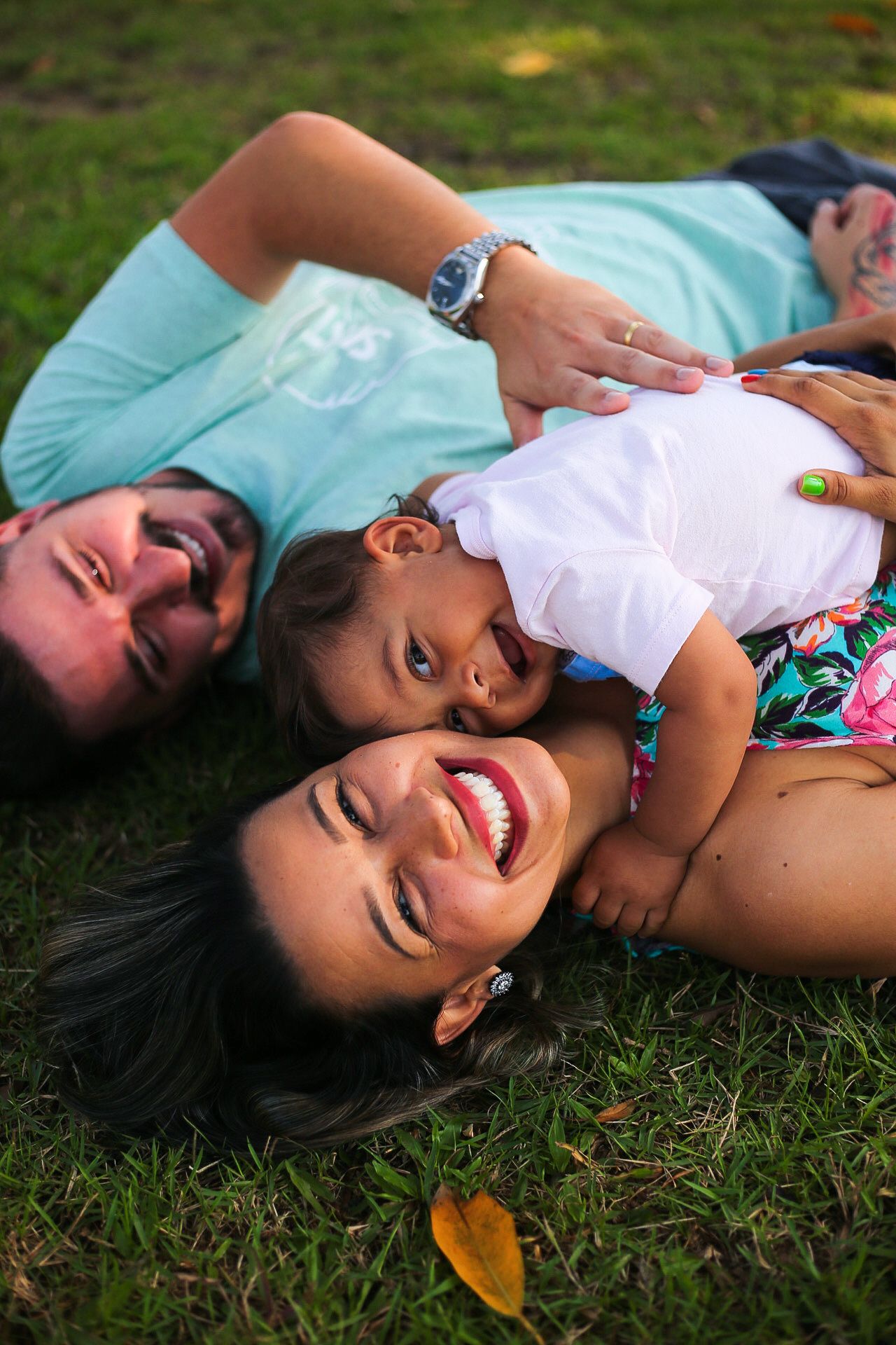 Three people lie on grass together laughing and smiling during an outdoor photo session.