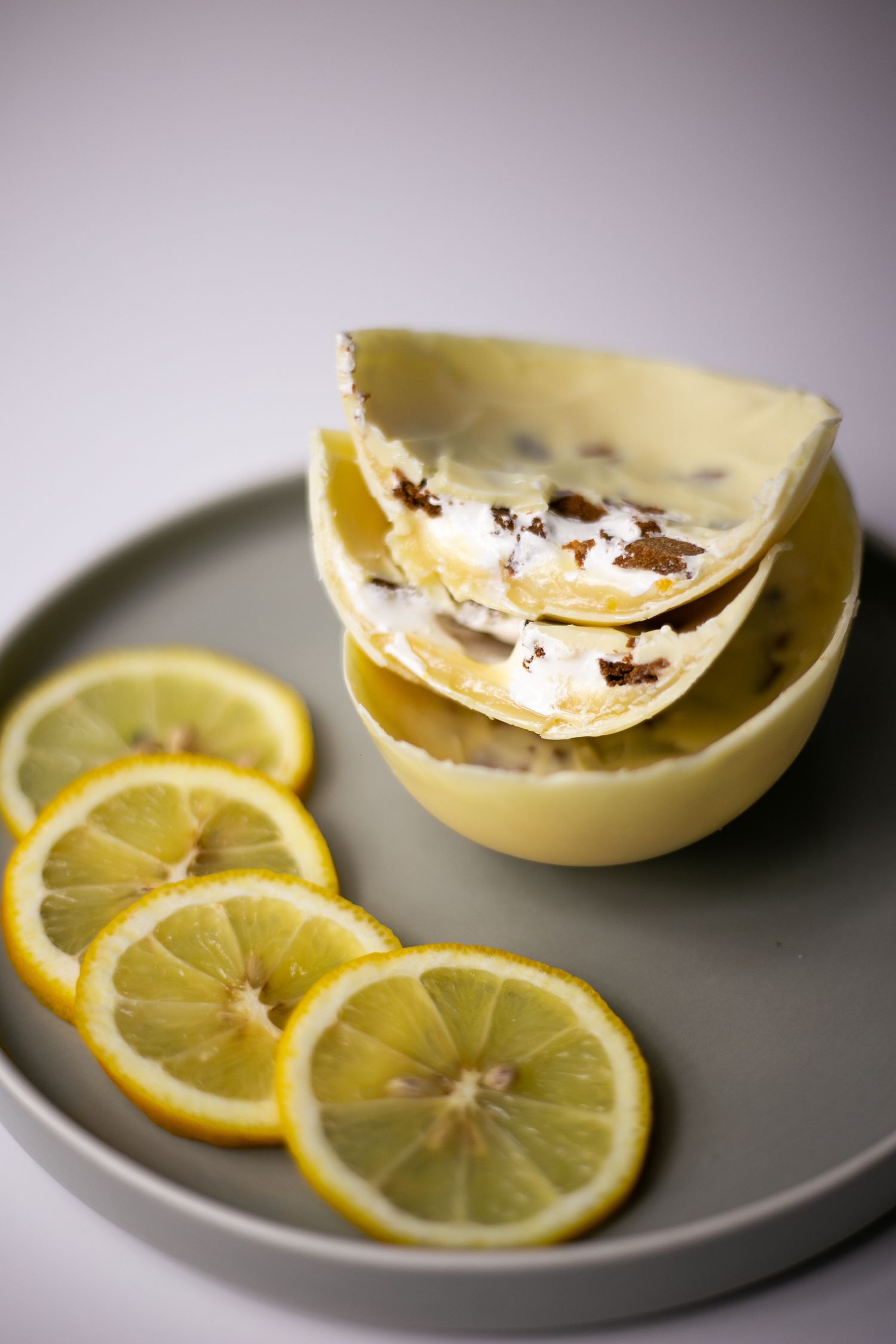 White chocolate shells filled with creamy filling stacked on a gray plate with fresh lemon slices.