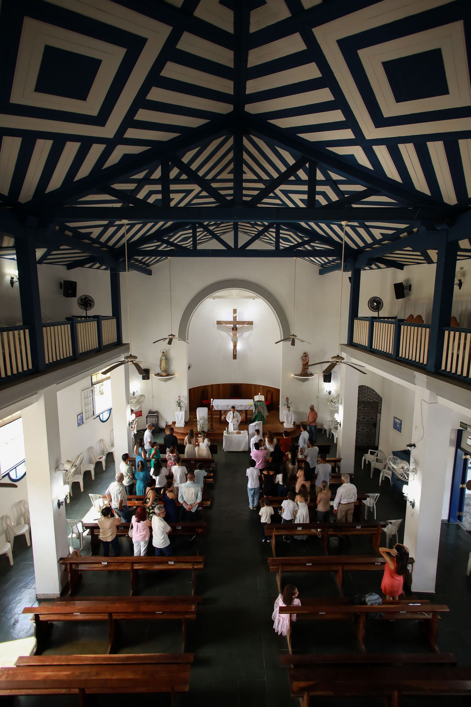 Aerial view of a church service inside a modern chapel with geometric black and white ceiling patterns and wooden pews.