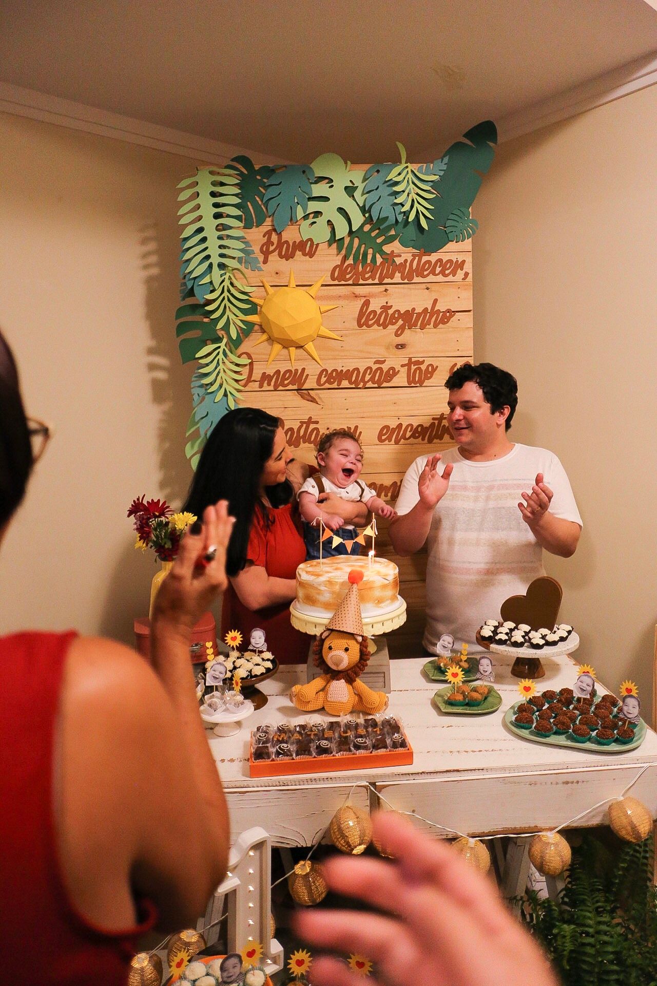 A tropical themed dessert table is set up for a celebration with cakes, treats and decorative palm leaf backdrop.