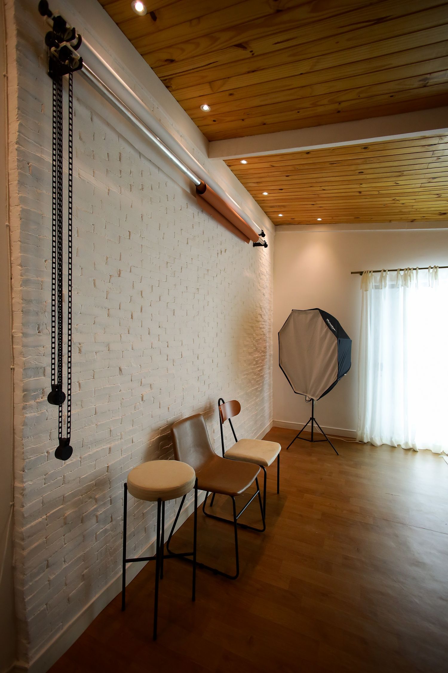 Modern photo studio interior with wooden ceiling, white brick wall and softbox lighting.