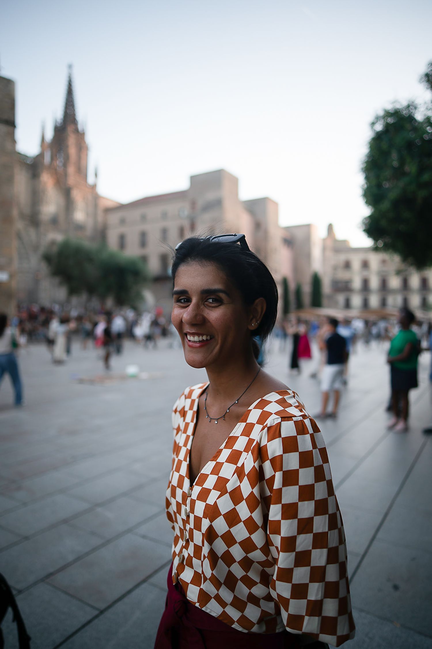 Person wearing orange and white checkered top smiles in front of European cathedral square.