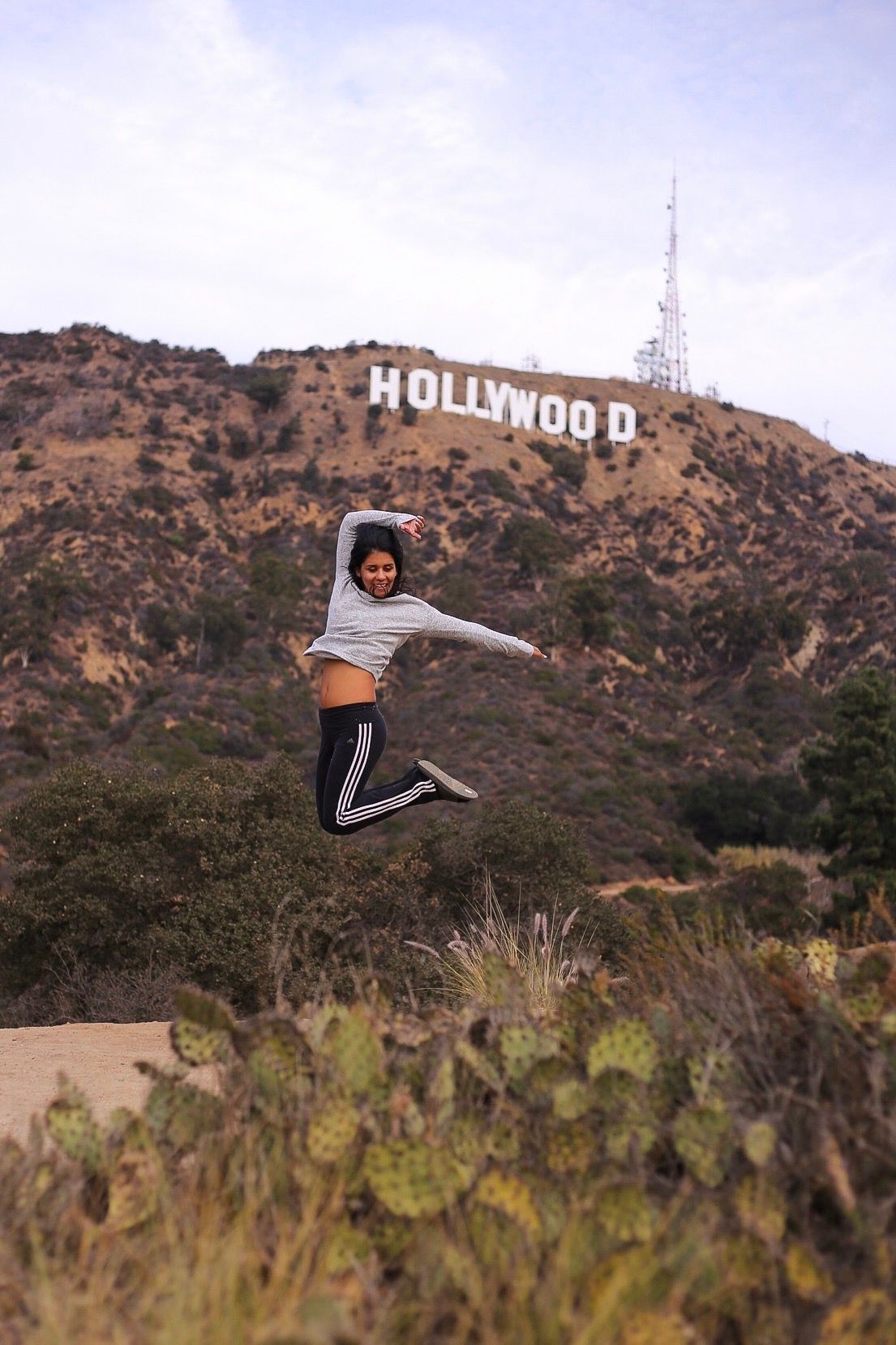 Someone leaps joyfully in front of the iconic Hollywood sign on a hill in Los Angeles, California.
