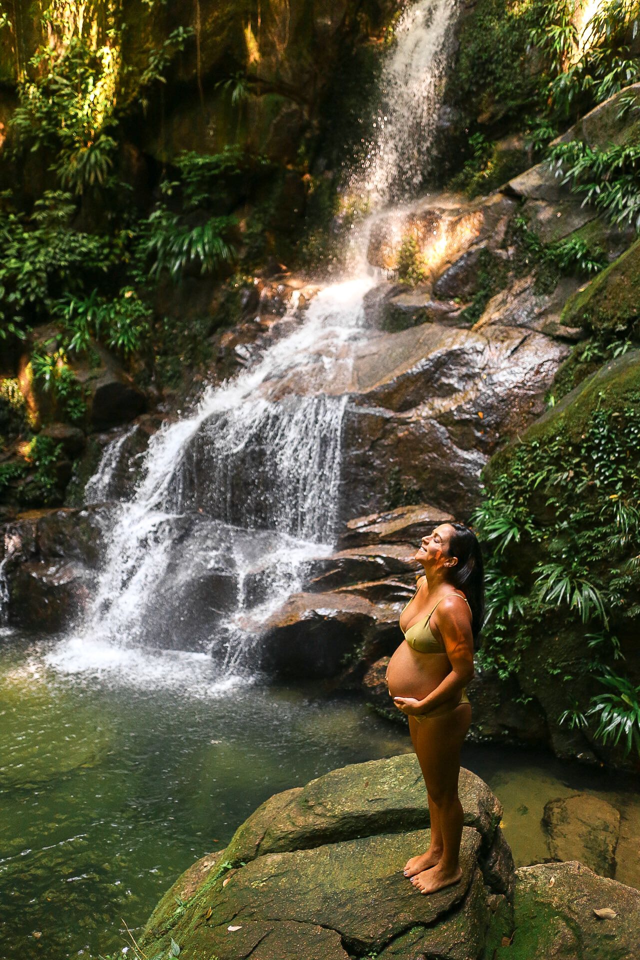 A scenic waterfall cascades into a pool surrounded by lush tropical vegetation in a serene forest setting.