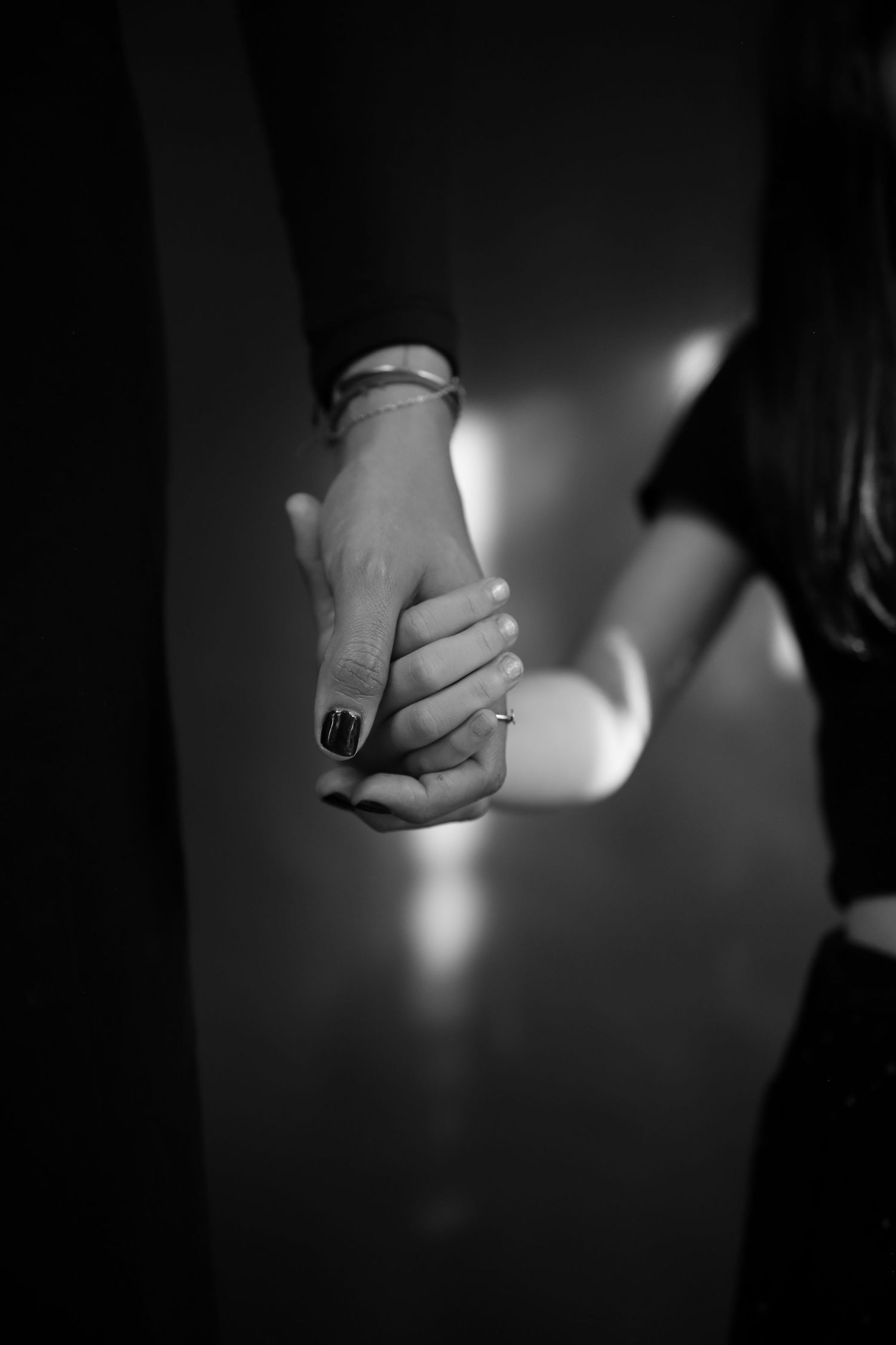 Black and white photo of a couple holding hands, woman wearing an engagement ring and bracelet.