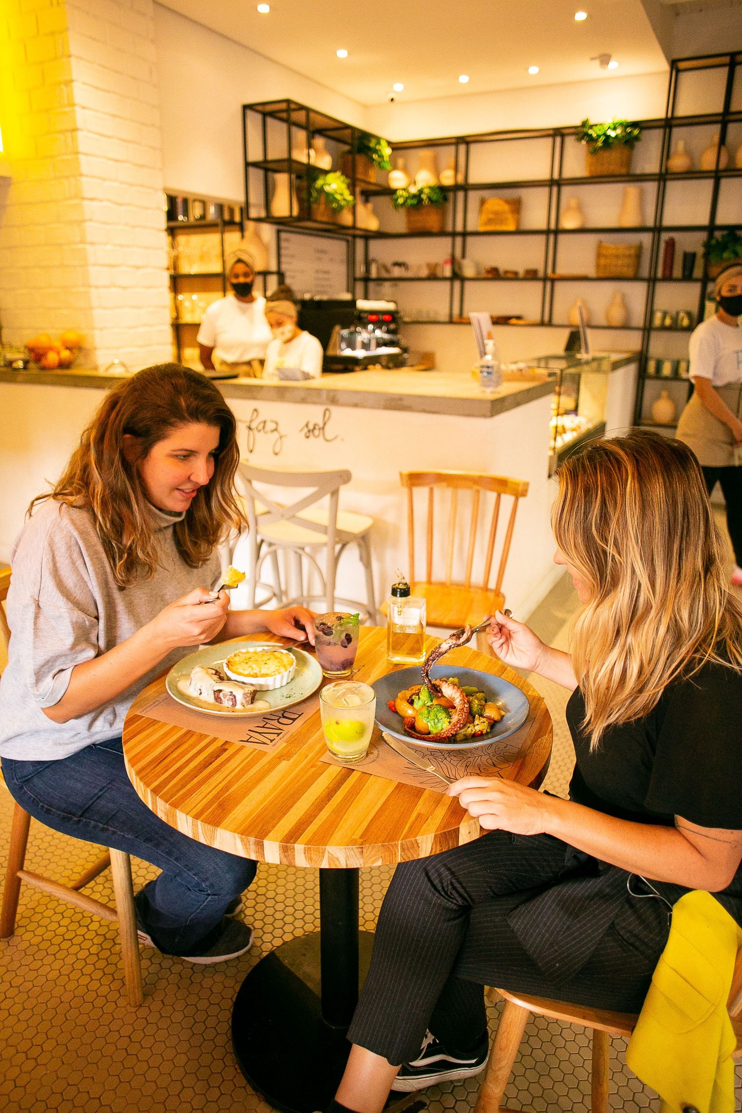 Two restaurant diners enjoying a casual meal at a round wooden table in a cozy cafe with modern decor.