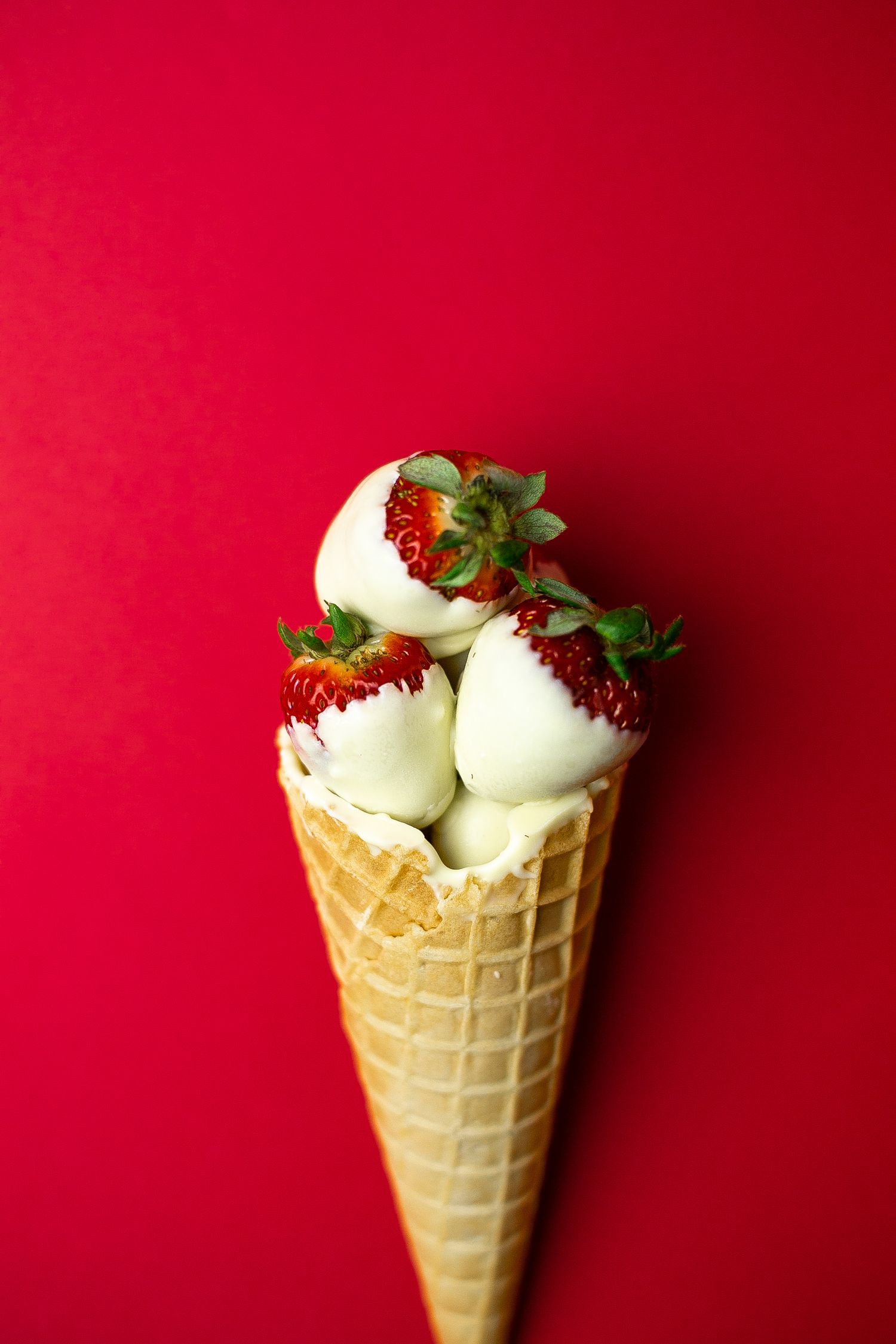 White chocolate covered strawberries arranged in a waffle cone against a vibrant red background.