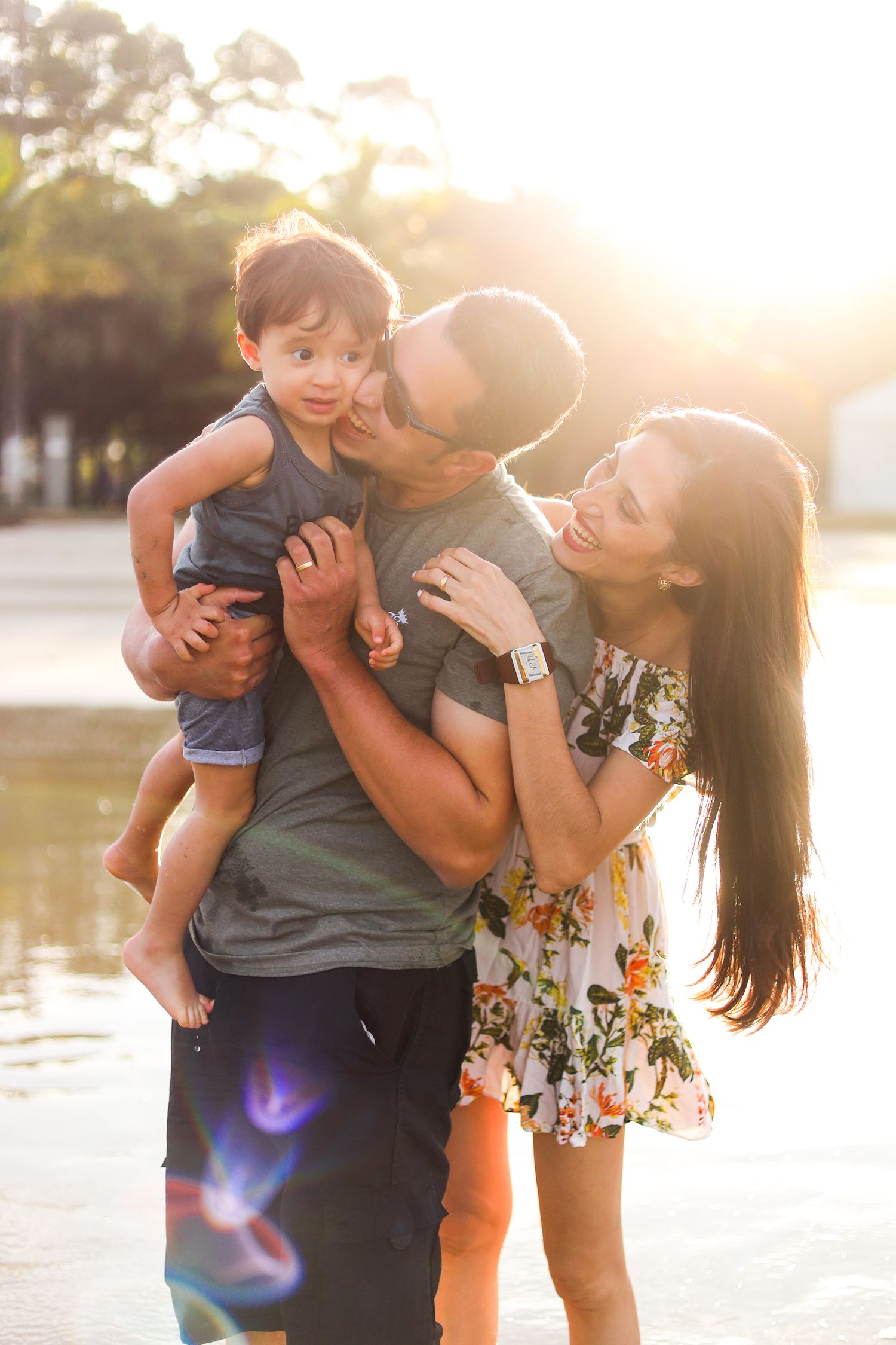 Family shares a joyful moment together outdoors during golden hour sunset with sunlight flare in background.