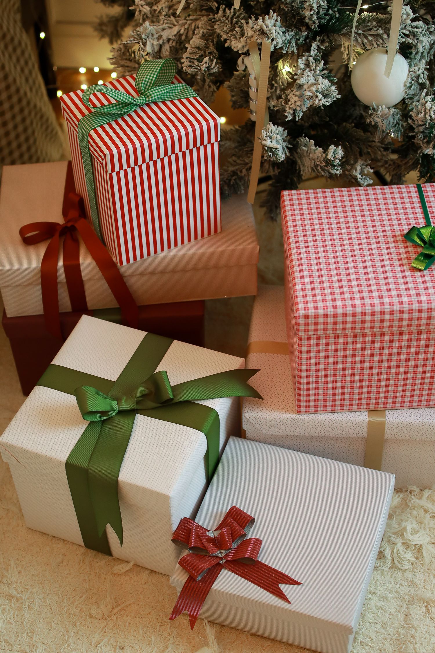 Festive Christmas presents wrapped in red and white striped paper with green and red bows sit beneath a decorated tree.