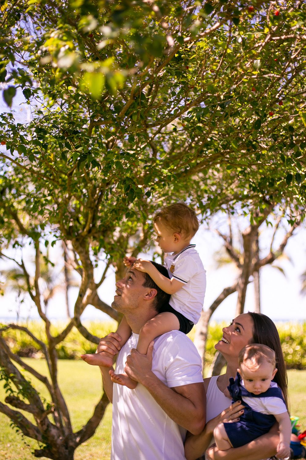 A family enjoying a sunny day outdoors under a leafy tree in white casual clothing.