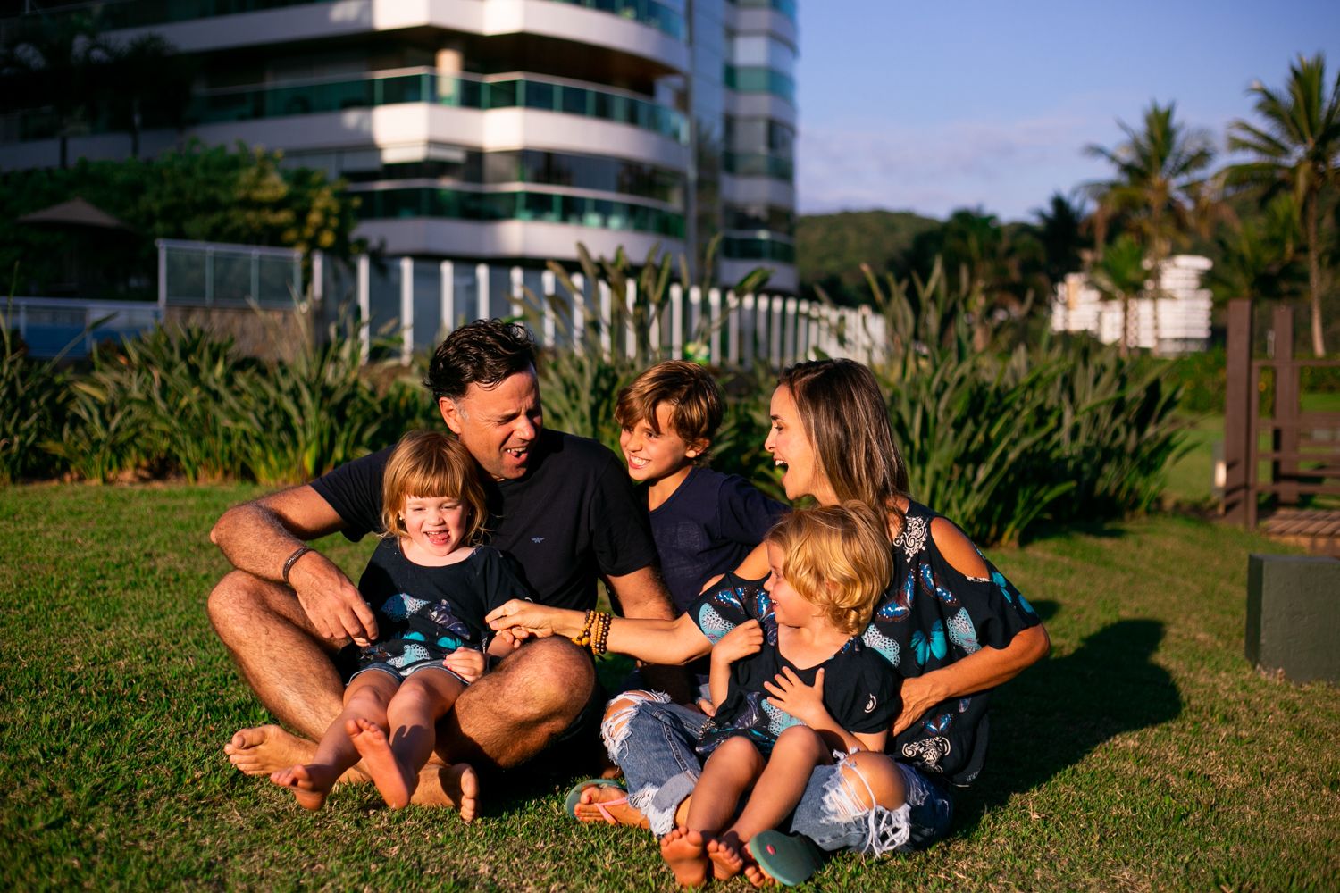 A family sits together on grass outside a high-rise building on a sunny day.