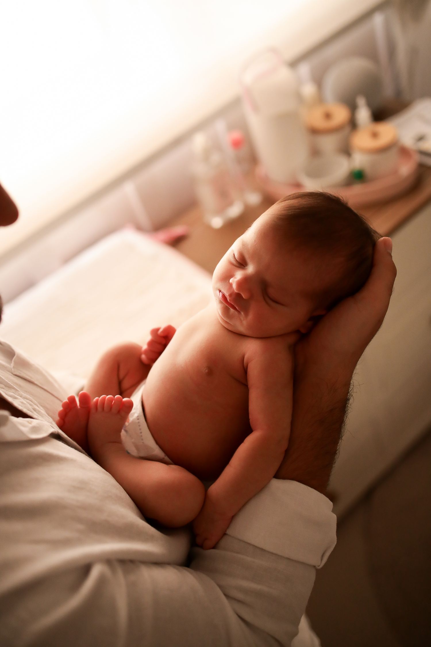 Peaceful newborn baby with closed eyes lying in white bedding in a warm, natural lighting setting.