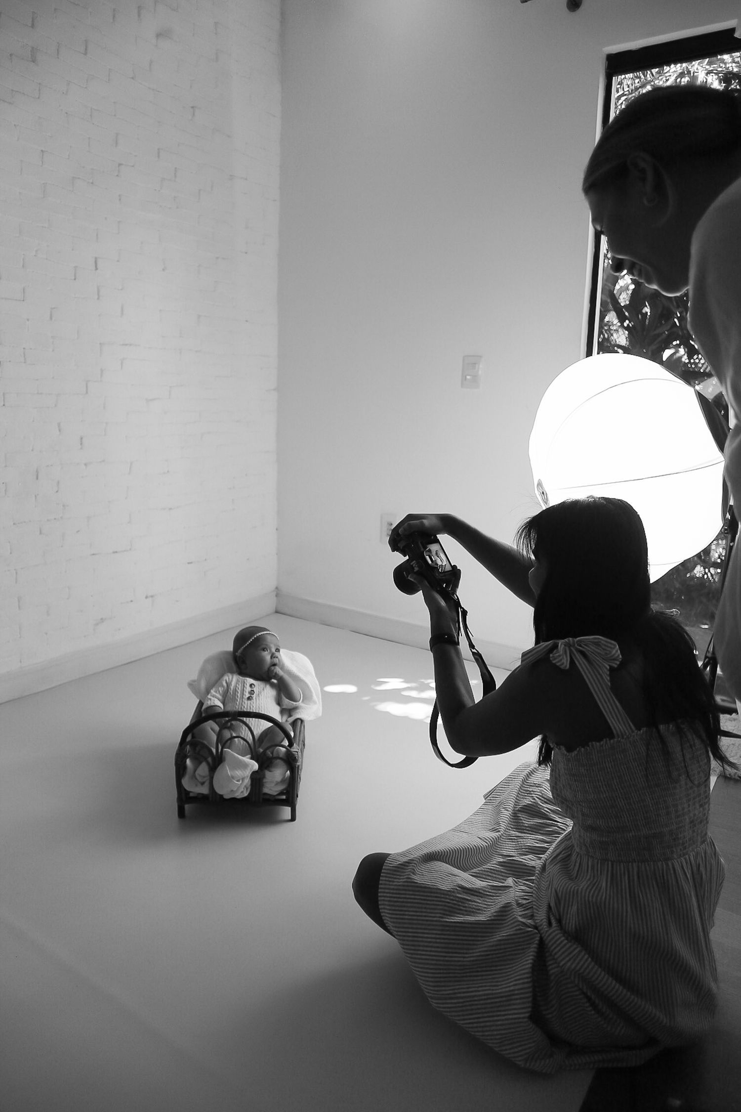 A photographer in white clothing takes pictures of a subject in a bright studio setting with natural lighting.