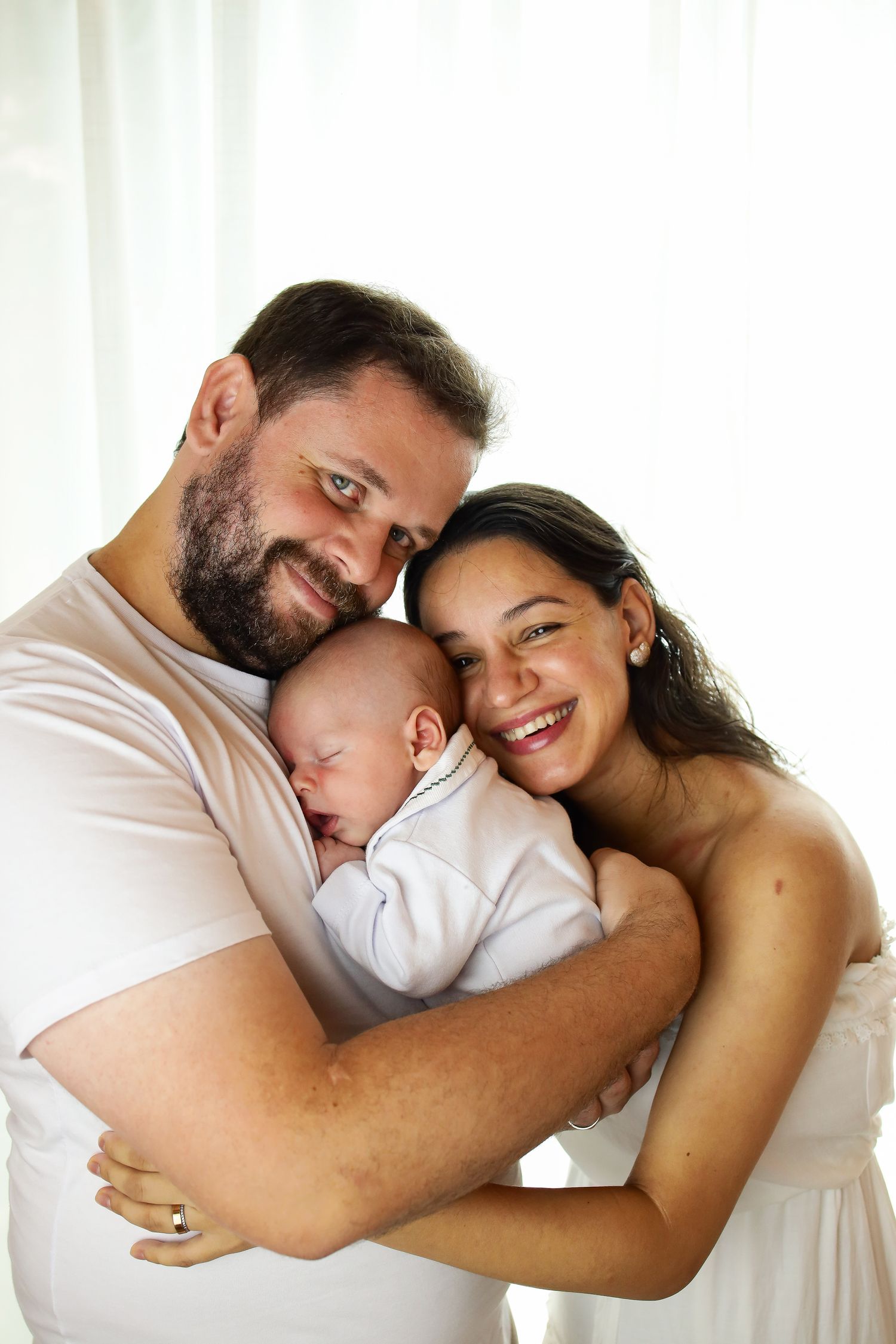 Happy family in casual white outfits cuddle together with sleeping baby at home in tender moment.