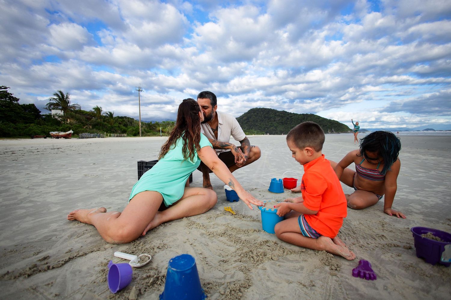 Children build sandcastles together at the beach on a sunny day with fluffy white clouds in the sky.