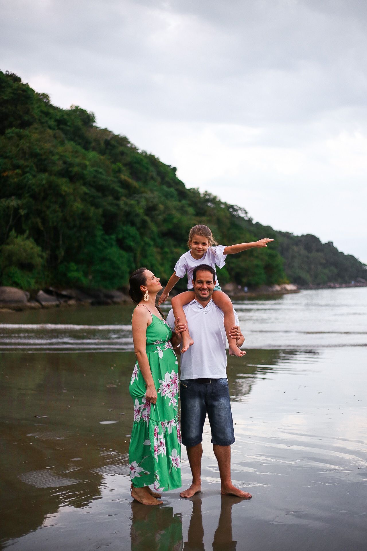 A family enjoys a peaceful moment together on a misty beach with lush green mountains in the background.