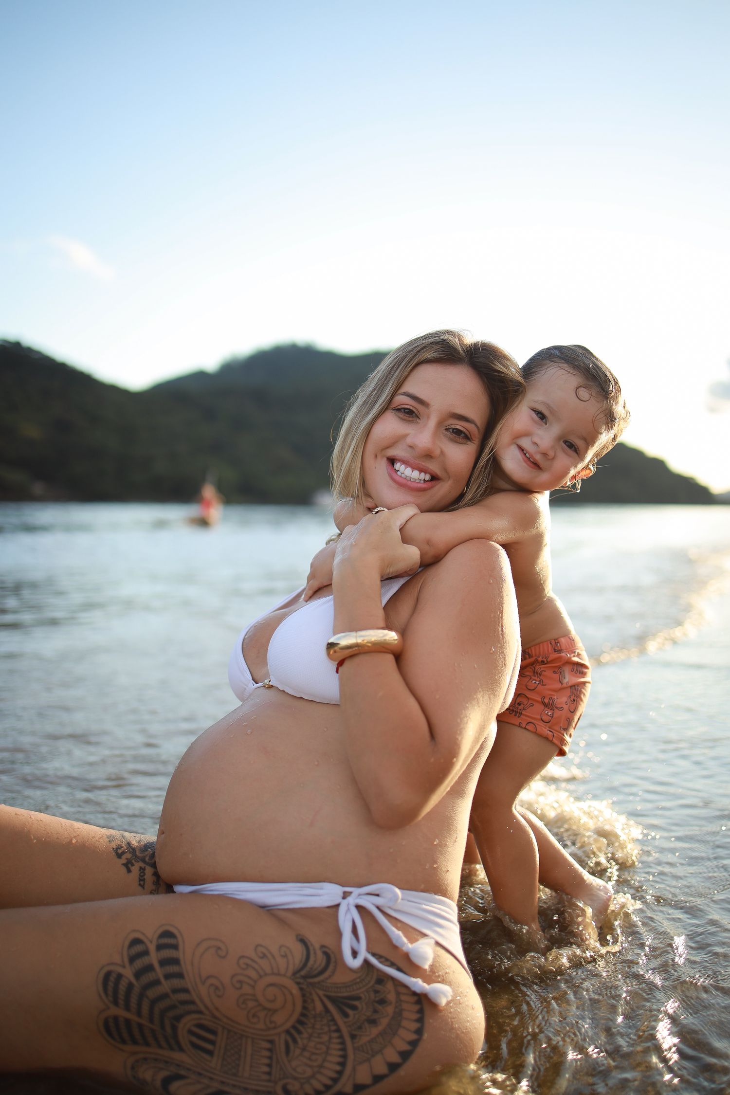 Mother and child playing in water with mountains and sunset in background.