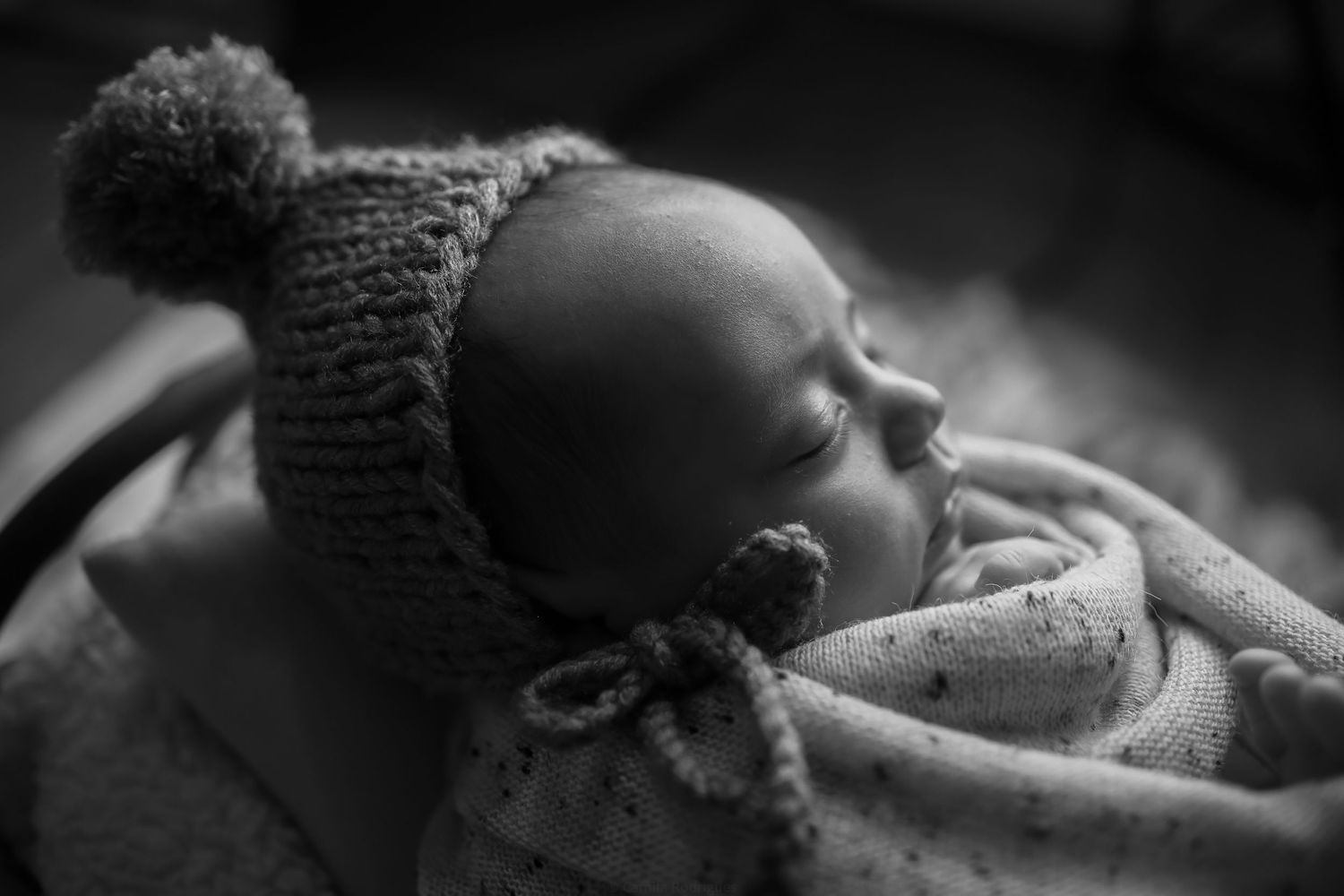 A peaceful sleeping newborn wearing a knit winter hat with pom pom in black and white photography.