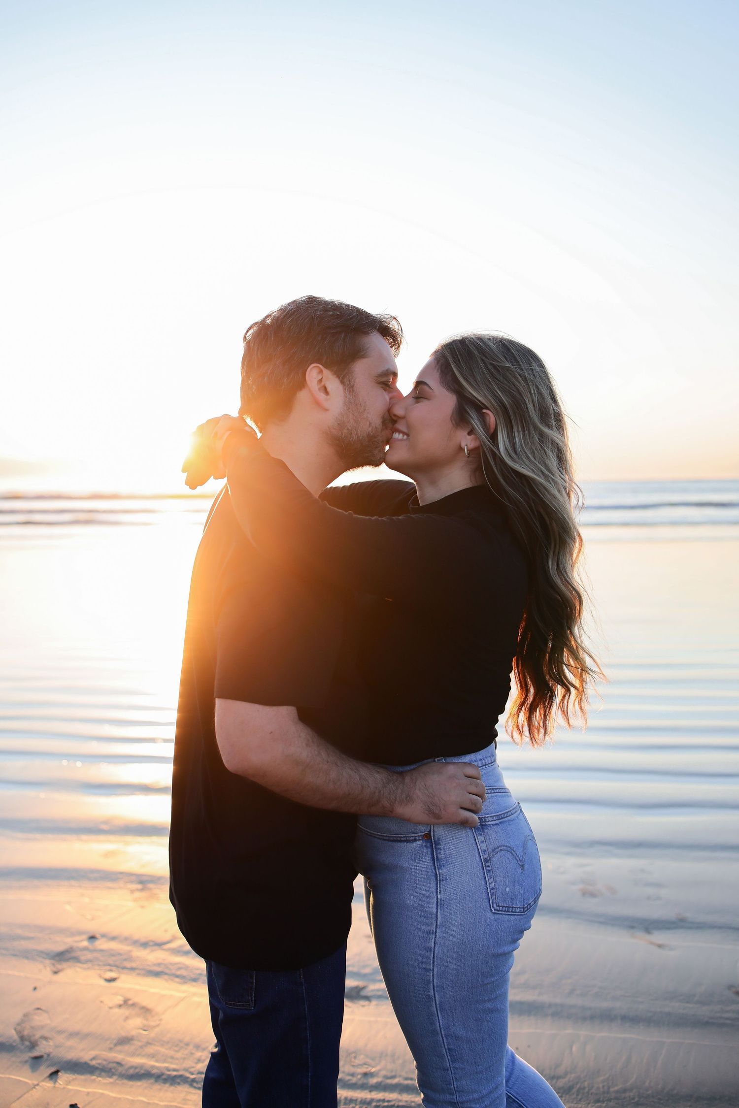 Romantic couple sharing an intimate moment on a beach at sunset with golden sun rays shining behind them.