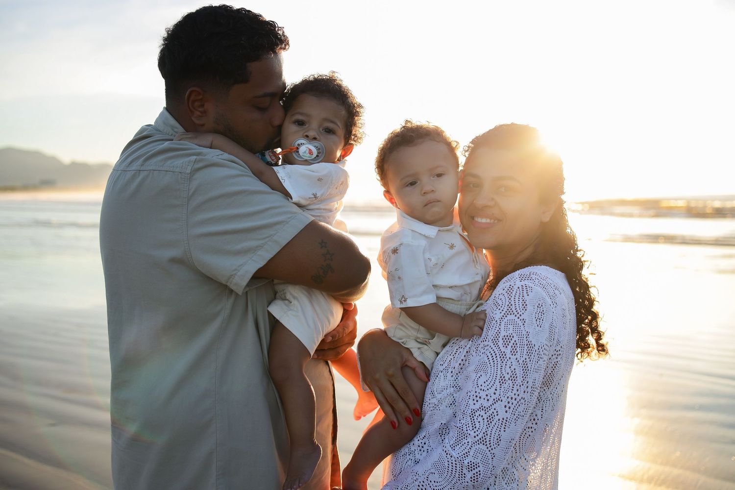 A couple shares tender moments with their baby during a golden sunset photo session at the beach.